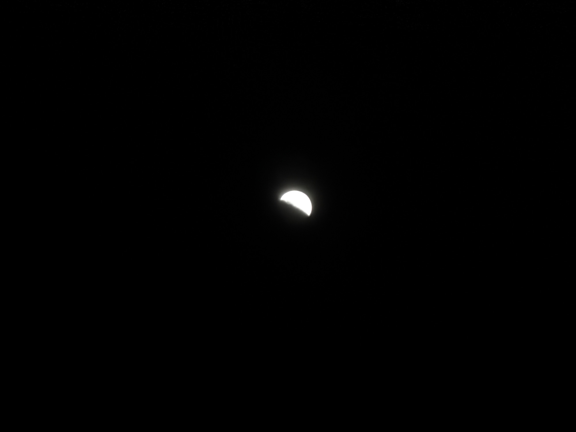 The image displays a close-up view of the moon against a completely black night sky. The moon is in a gibbous phase, with slightly more than half of its disc brightly illuminated on the right side, creating a distinct crescent-like but fuller shape. The illuminated portion glows intensely, standing out sharply against the deep darkness of the surrounding space. The left side of the moon remains in shadow. No stars, clouds, or other celestial bodies are visible in the background, emphasizing the moon as the sole subject. The image suggests a clear night, free from atmospheric interference. No surface details of the moon, such as craters or maria, are clearly discernible. The photograph captures a serene astronomical view during nighttime. The location context provided for this image is Izhevsk, Russia. There is no visible text in the image.