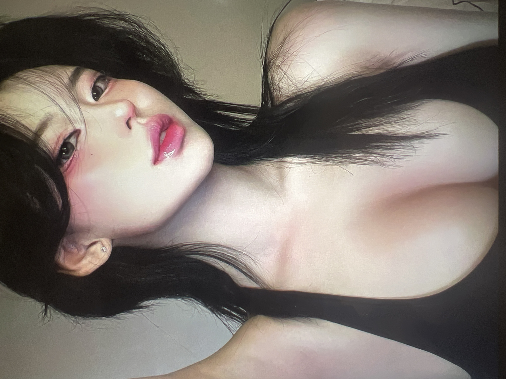 The image is a close-up, chest-up portrait of a young woman with dark hair, fair skin, and heavy makeup. She is wearing a black top. Her eyes are dark, and she has pink blush and pink lipstick. Her hair is long and dark, framing her face and falling over her shoulders. The background is a neutral, light color, suggesting an indoor setting. There are no discernible elements that would indicate a specific location in Minsk, Belarus.