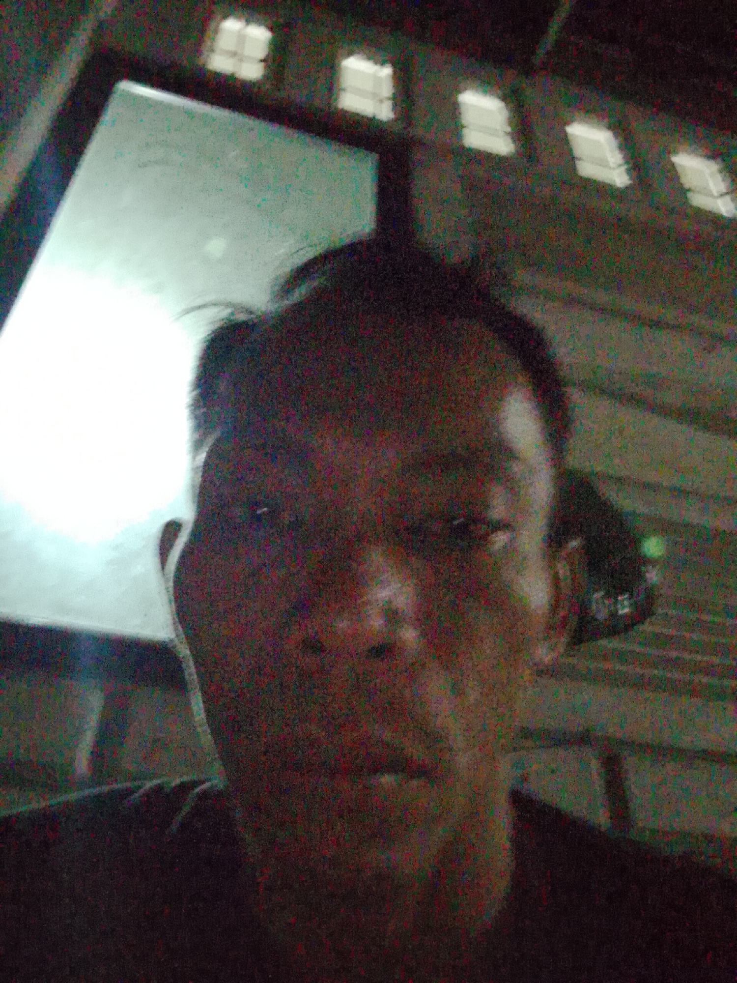 A poorly lit, grainy photograph depicts a person facing the camera. The location is likely indoors, based on the visible light fixtures or windows in the background. No specific details confirm the location is Bukit Ketok, Indonesia.
