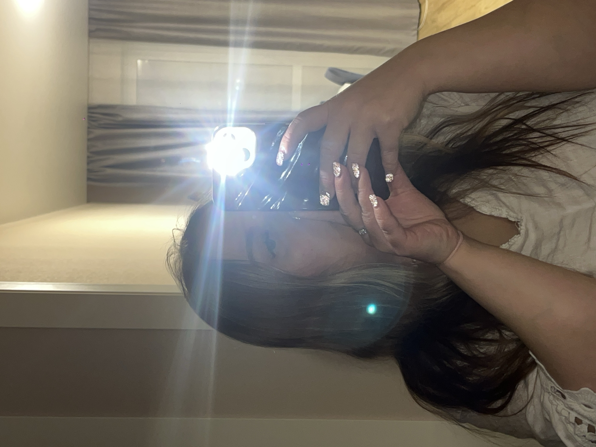 A person is taking a selfie with a smartphone, illuminated by the phone's flash. The background includes curtains and a wall. It's not possible to discern the location in Krasnodar, Russia, from the given image.