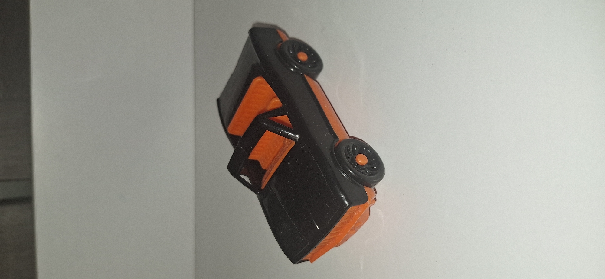 A black and orange toy convertible car is displayed on a white surface. The car has an orange interior and wheels. The background is a plain white wall. The image appears to have been taken indoors in a studio setting. No specific location in Bila Tserkva, Ukraine is identifiable from the image.
