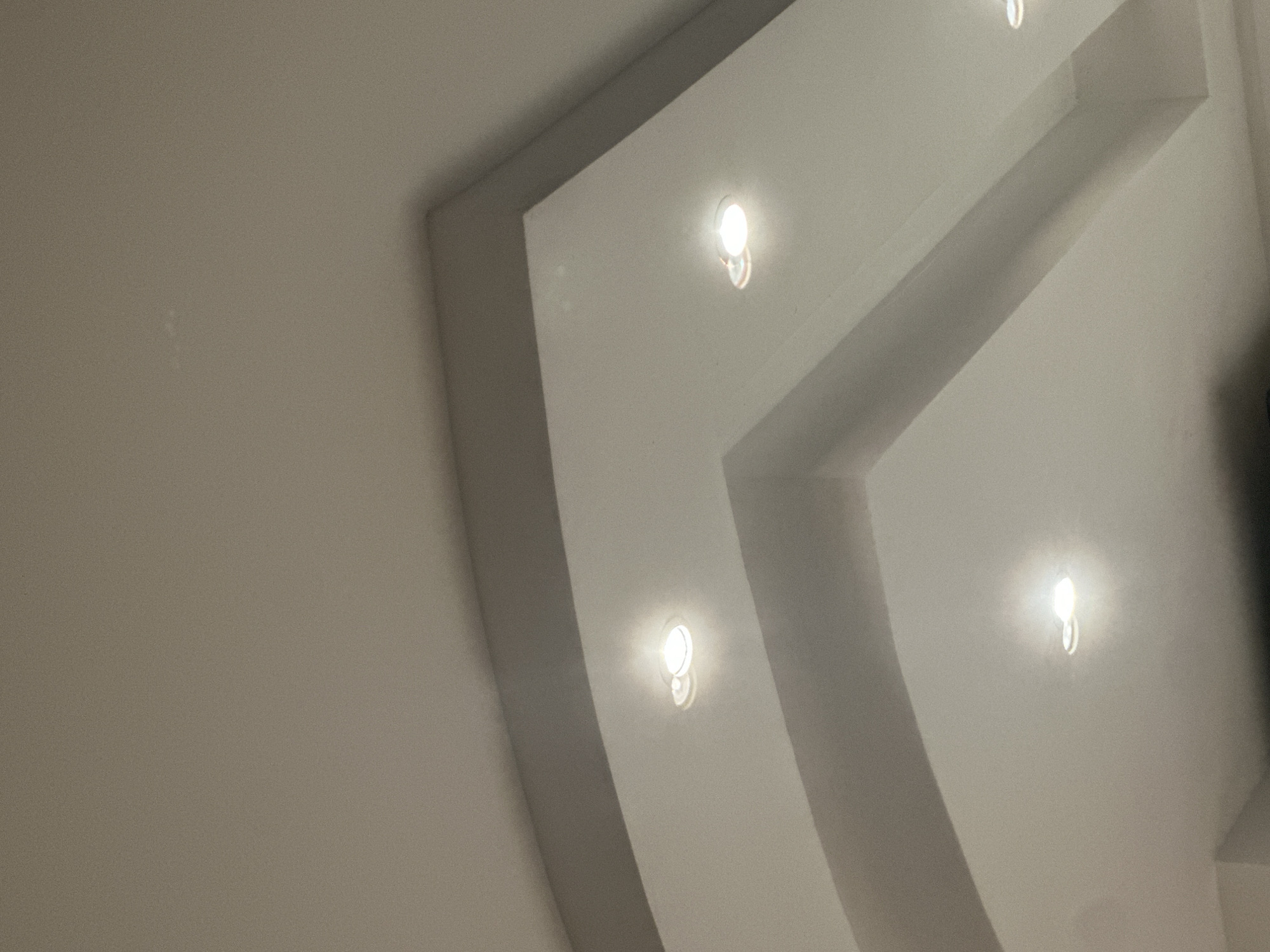 The image shows a section of a white ceiling with inset lighting. The ceiling has a stepped, recessed design, with lights placed within the recessed areas. There are no people visible. The location is impossible to determine as it is not within the field of view.
