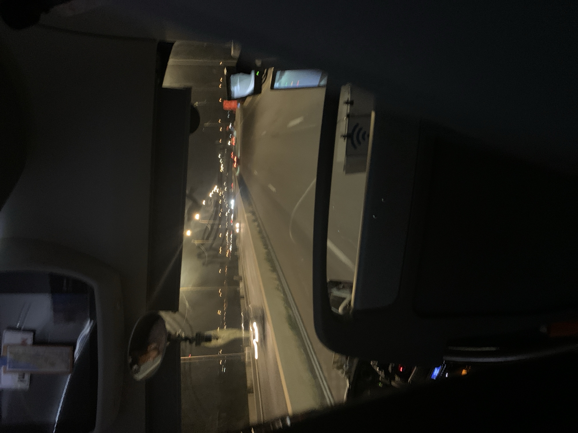 The image depicts a view from inside a vehicle, possibly a truck, at night. The vehicle appears to be on a highway with heavy traffic, indicated by the blurred streaks of headlights and taillights of other vehicles. The highway is divided by lanes. The interior of the vehicle is visible, showing the dashboard, rearview mirror, and possibly other in-cab equipment. A traffic signal is visible in the distance, which can not be used to conclude where this photo was taken. The image is rotated, so the traffic appears to be moving vertically. Without additional information, it is impossible to determine the precise location of the image, including if it is in Tel Aviv, Israel.