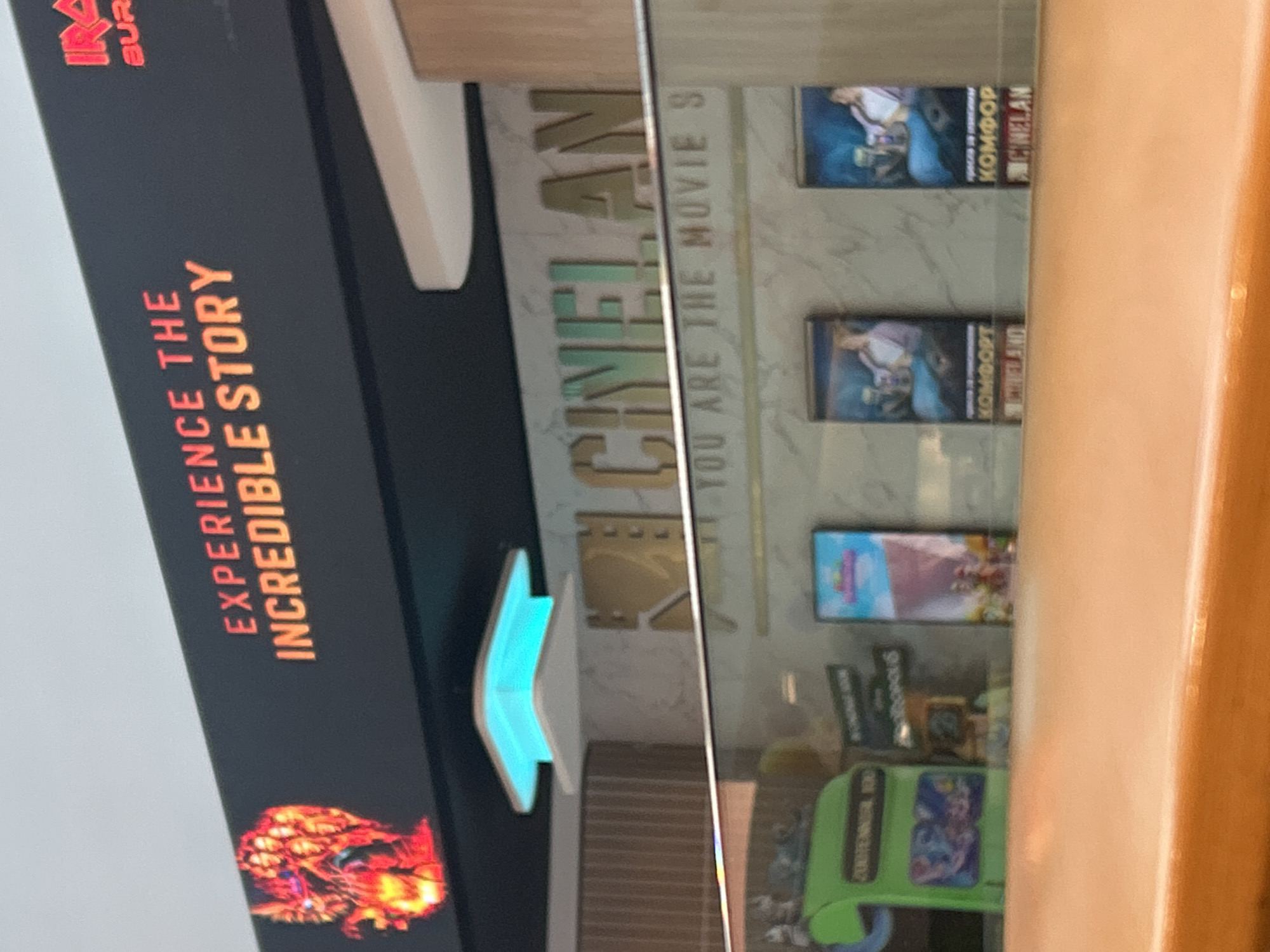 The image shows a sign that reads "EXPERIENCE THE INCREDIBLE STORY" and "CINELAND" with the text "YOU ARE THE MOVIE S" on a wall in Varna, Bulgaria. Several movie posters are mounted on the wall under the lettering.