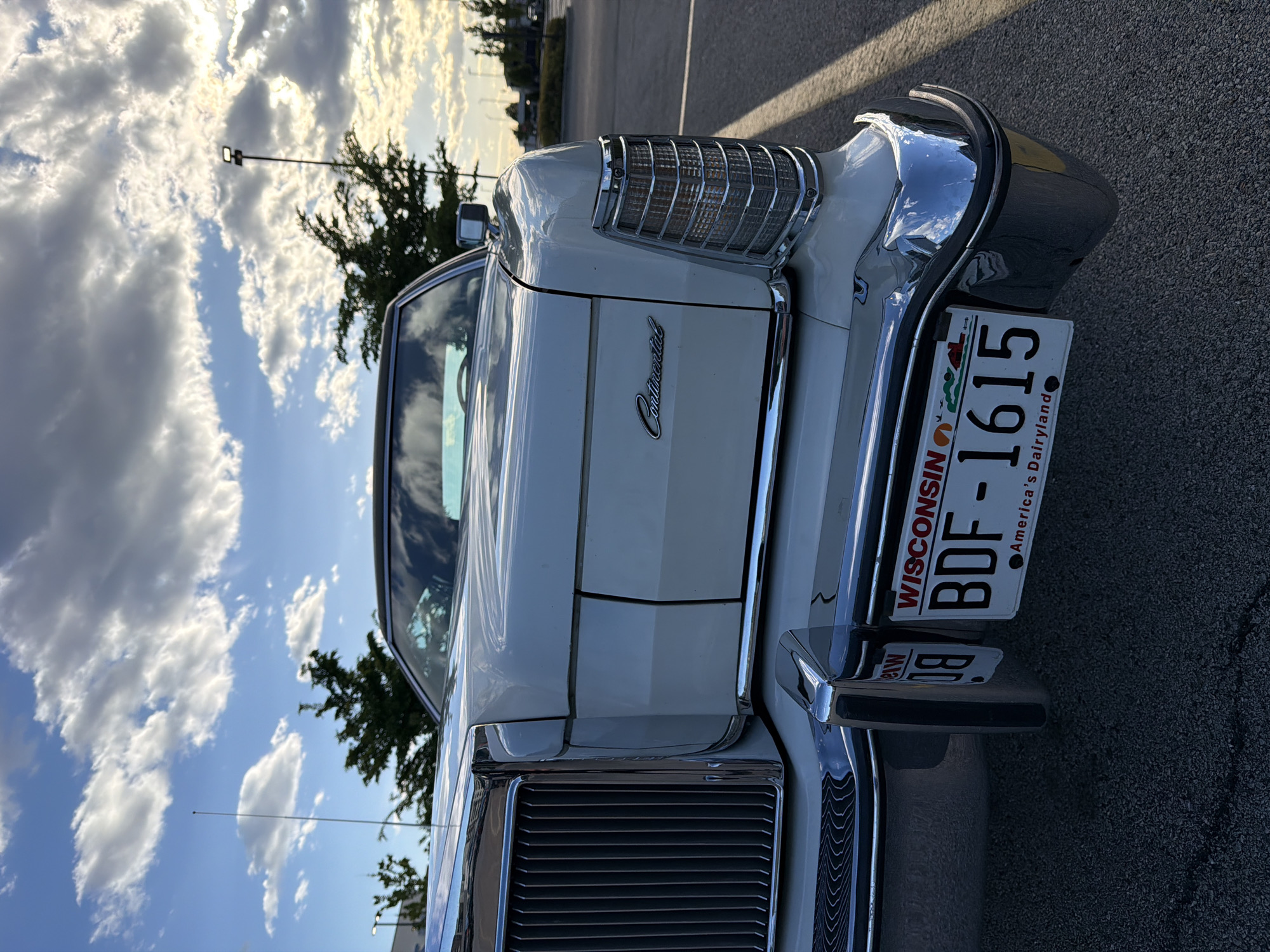 The image shows the front of a white Continental car. The car has a Wisconsin license plate that reads "BDF-1615" with the slogan "America's Dairyland." The sky is visible in the background with clouds and a light pole. The photo appears to be taken in a parking lot. The location cannot be confirmed as Morton Grove, United States of America, without further visual or contextual evidence.