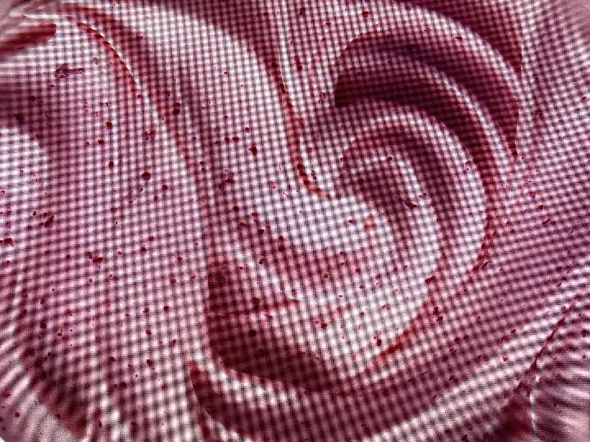 A close-up image shows a swirl of pink cream or frosting with dark specks distributed throughout. The texture appears smooth, with ridges and curves indicating a swirl pattern. The dominant color is pink, with varying shades creating depth and dimension in the swirl. The overall composition suggests a dessert or confectionery item. There is no evidence in the image to indicate the location or any elements associated with Poltava, Ukraine. The scene does not depict people, specific actions, or interactions.