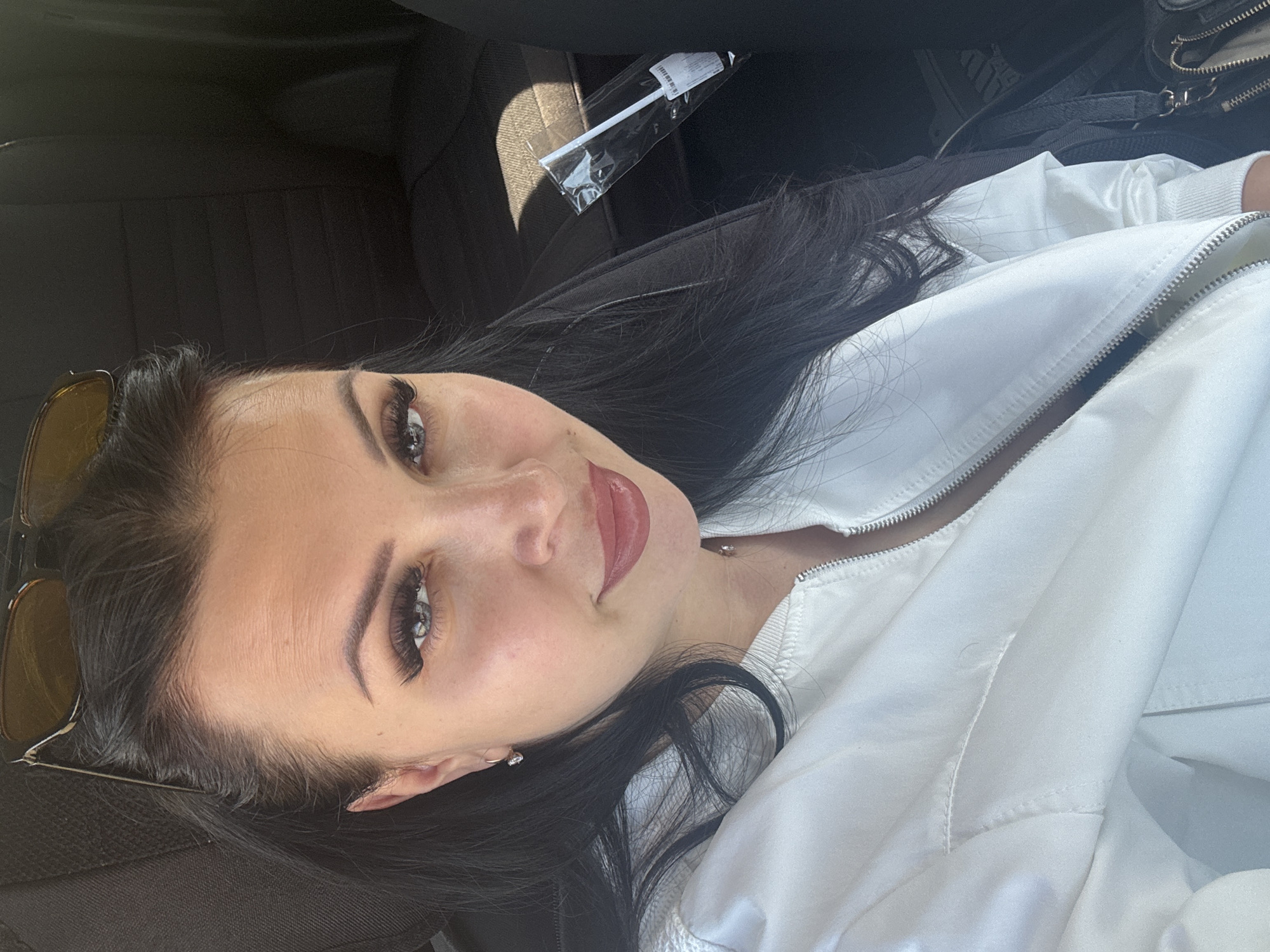 A woman is in what appears to be a car. She's wearing a white jacket. Sunglasses are positioned near her face. In the background, there's a plastic-wrapped item and a black bag. There is no information to determine if this photo was taken in Vladivostok, Russia.