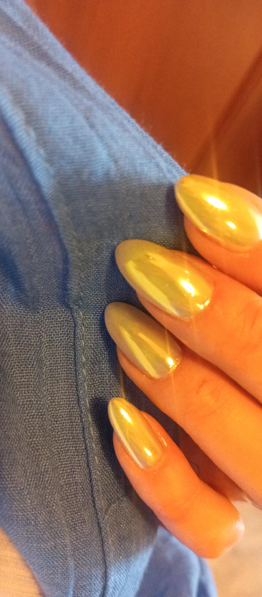 A hand with gold-colored, almond-shaped nails rests on a blue fabric. No city or location is discernible.
