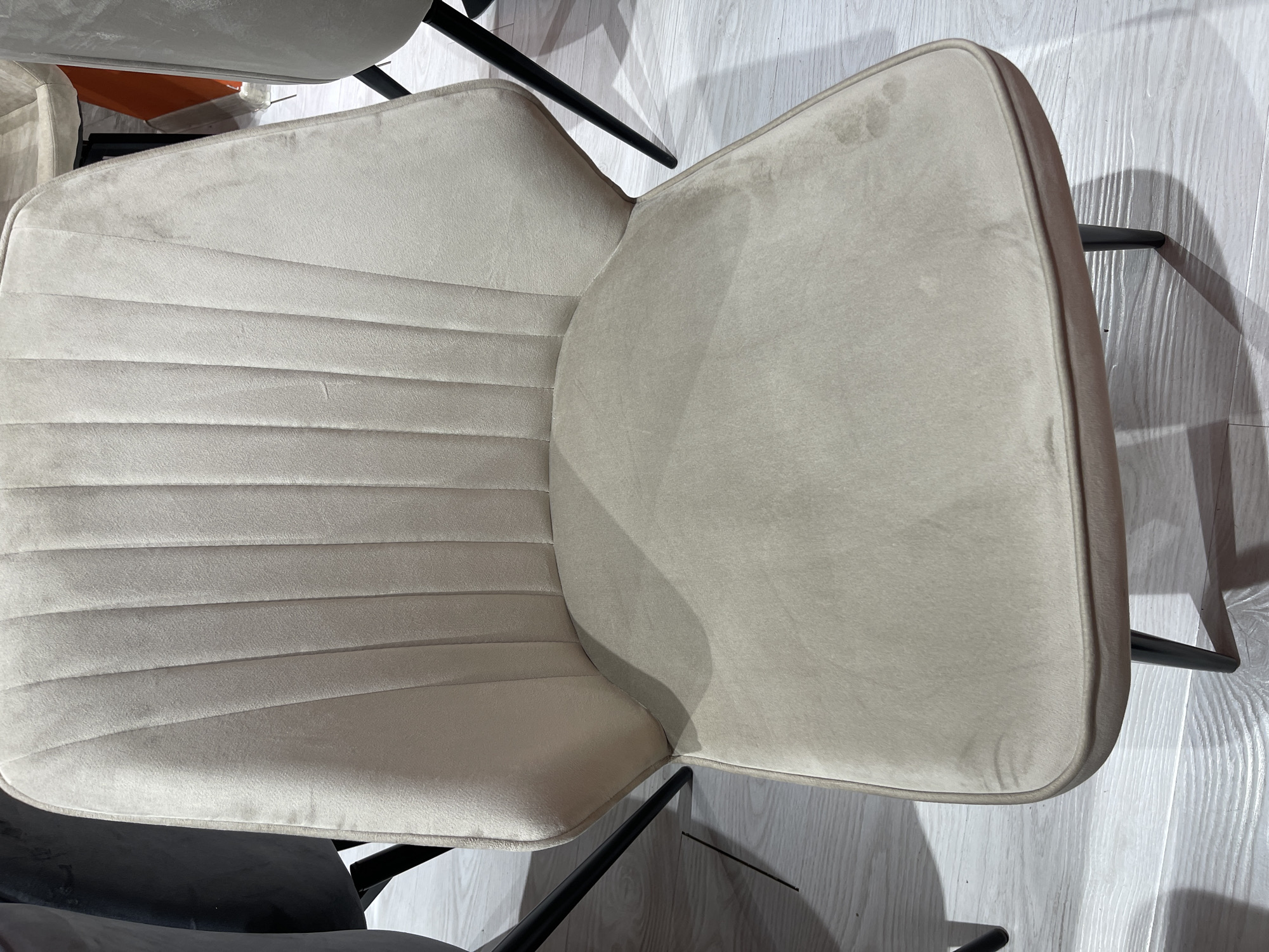 The image shows a close-up view of a light beige upholstered chair with a channel-tufted back. The chair has dark, slender legs. The chair appears to be in a retail or showroom setting, with other chairs and furniture visible in the background, as well as a light-colored wooden floor. The overall impression is of a modern and stylish interior. There is no specific information in the image to indicate its location in Moscow, Russia.
