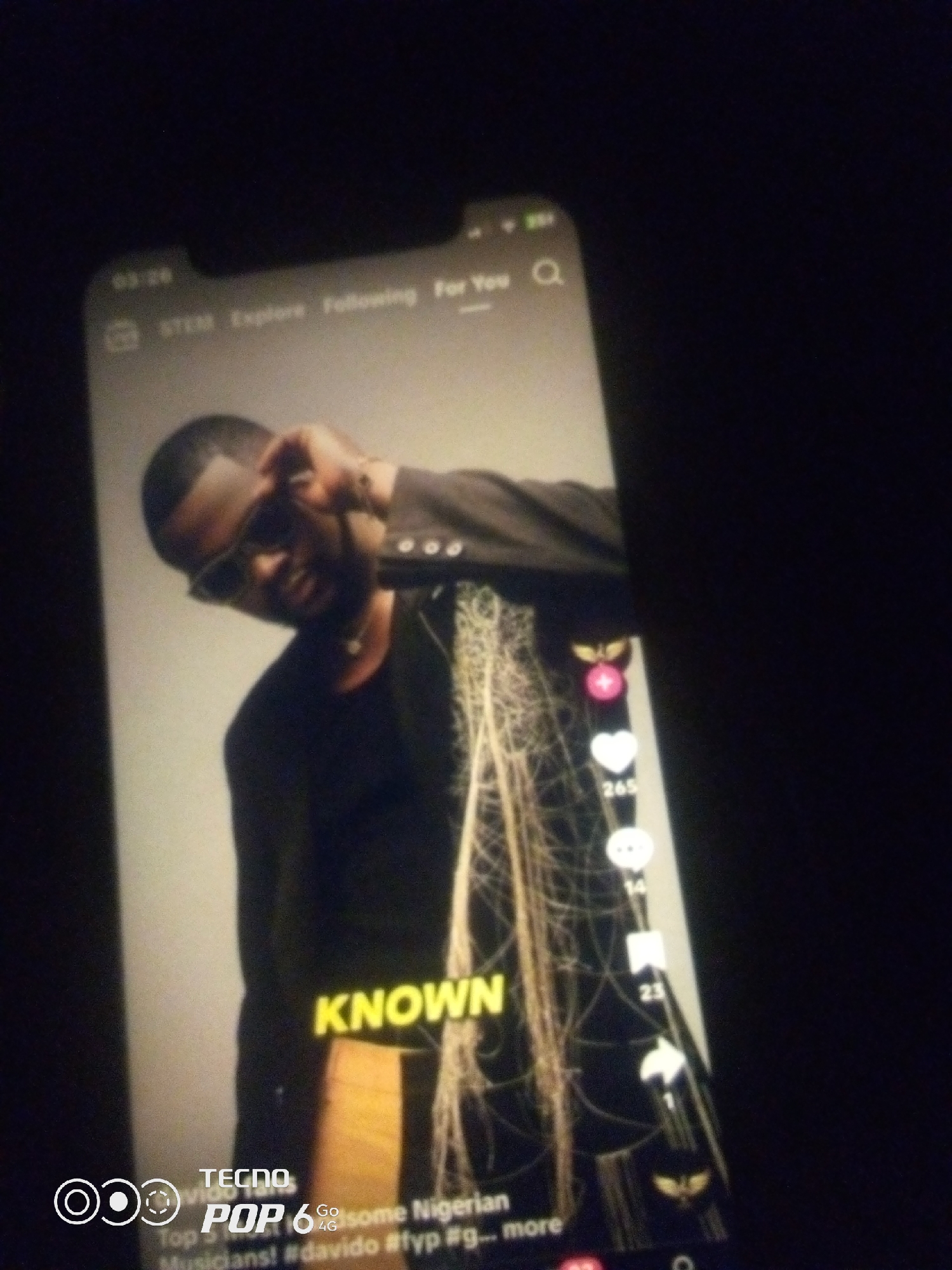 The image shows a close-up of a smartphone screen displaying a social media video. The video features a man wearing sunglasses and a dark outfit. Text overlays on the screen include "KNOWN" in large yellow letters, and below it, "Top Go some Nigerian Musicians! #davido #fyp #g... more". The bottom left corner of the screen displays a TECNO POP 6 Go logo. The phone is held in a dark environment, likely indoors. There is no visible indication of the city of Howayi, Nigeria.