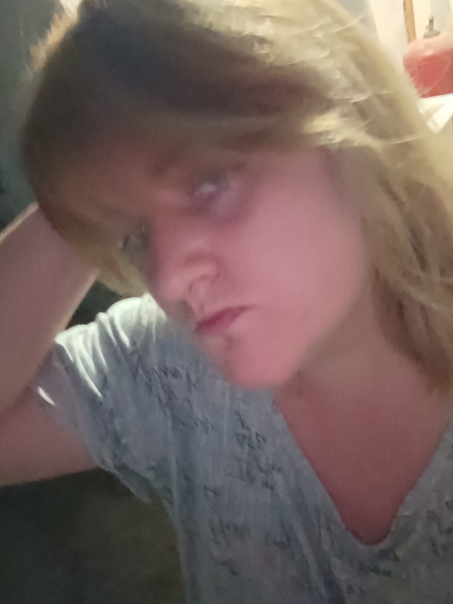 A close-up selfie of a light-skinned person with shoulder-length blonde hair. The person's left arm is raised, with their hand near their head. They are wearing a light-colored patterned shirt. The background is indistinct but appears to be indoors. No location information pertaining to Верхнесадовский округ, Ukraine, can be derived from the image.