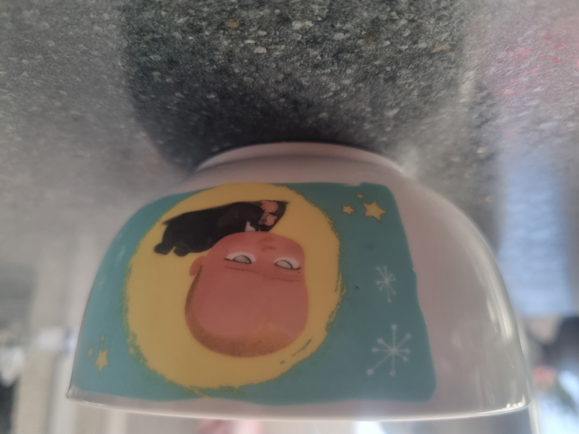 The image shows a close-up of a white ceramic bowl featuring a cartoon image of the character "The Boss Baby". The character is depicted lying down, wearing a black suit and tie. The background of the image on the bowl is a teal color with yellow stars and white snowflake-like designs. The bowl is placed on a dark, speckled countertop. There is no indication of the city of Samara, Russia, or any environmental details beyond the immediate foreground.