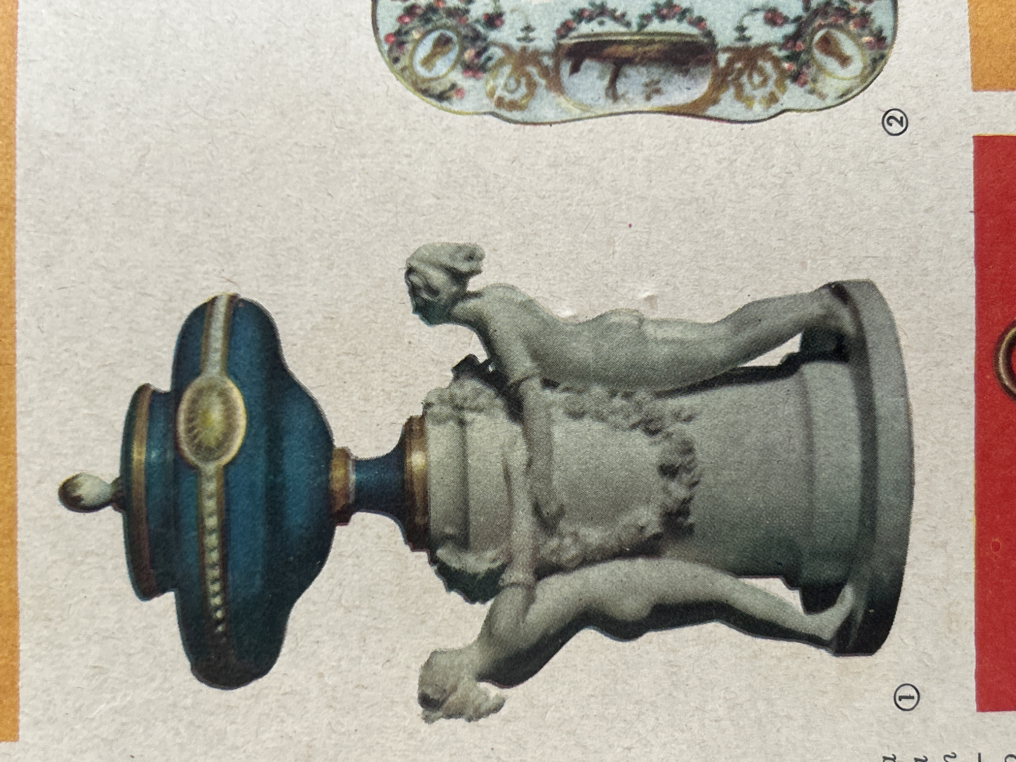 The image shows a decorative blue and gold urn-like object with two sculpted figures embracing its base. The object is mounted on a pedestal. To the right, a portion of another decorative item with floral patterns is visible. The background is a light-colored, textured surface, possibly paper. The image appears to be a reproduction or a page from a catalog or book, indicated by the presence of circled numbers "1" and "2" and a red band at the bottom. The scene is static and offers no information about the city of Santa Ana, Venezuela.