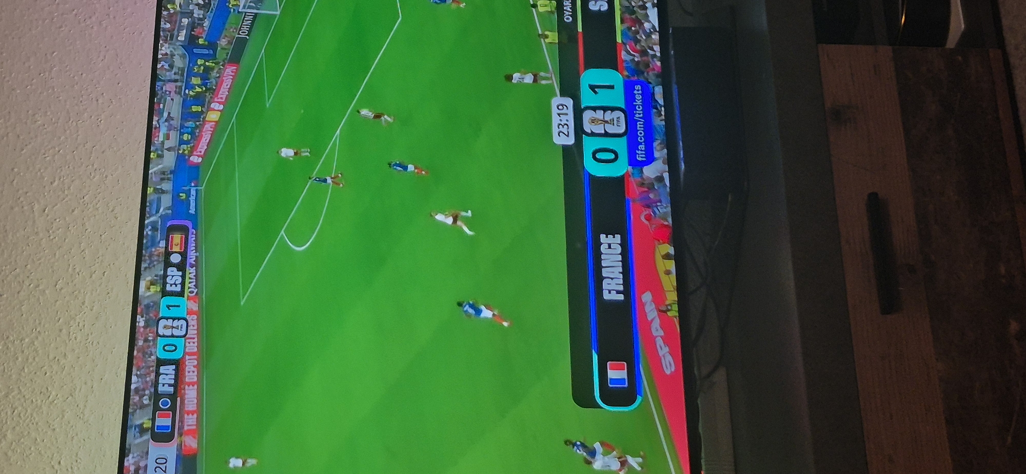 This is a photograph of a television screen displaying a soccer match between France and Spain. The score is 0-1, with Spain leading. The time displayed is 23:19. The bottom portion of the screen shows a banner with "FRANCE" on the left and "SPAIN" on the right, with the score in between. There are also advertisements visible along the bottom and sides of the screen, including "THE HOME DEPOT DELIVERS", "QATAR AIRWAYS", and "ExpressVPN". The stadium seating is visible in the background, filled with spectators. The image was taken in Baden-Baden, Germany.