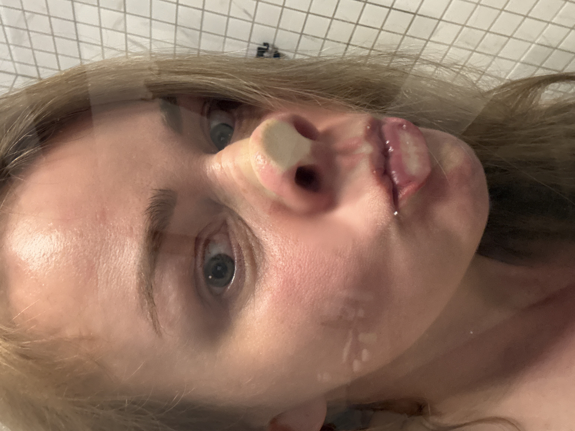 The image shows a close-up, slightly angled view of a blonde woman's face against a background of small, light-colored tiles. There are droplets or streaks visible on the face and what appears to be a reflection overlaying the image, creating a diffused effect. No information is available regarding the city of Saint Petersburg, Russia.