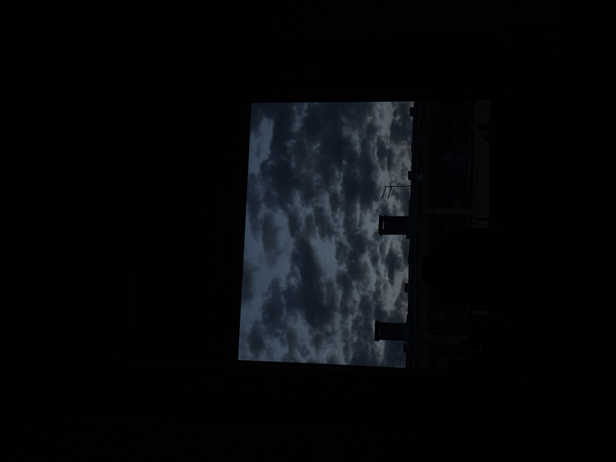 The image depicts a view of a cloudy sky above buildings in Kragujevac, Serbia. The buildings appear silhouetted against the sky, suggesting a dark or nighttime scene. The sky is filled with dense, dark clouds, indicative of inclement weather. The overall scene is somber and lacks distinct details due to the low lighting.