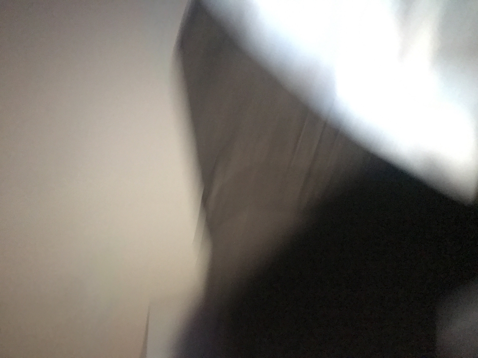 The image is blurry and indistinct, showing a light-colored wall on the left and a darker, possibly brown or black, shape on the right. There is also a bright area, possibly due to light, in the upper right corner. Due to the lack of clarity, it is impossible to determine a specific location in Yerevan, Armenia, or any other details about people, subjects, objects, or actions.