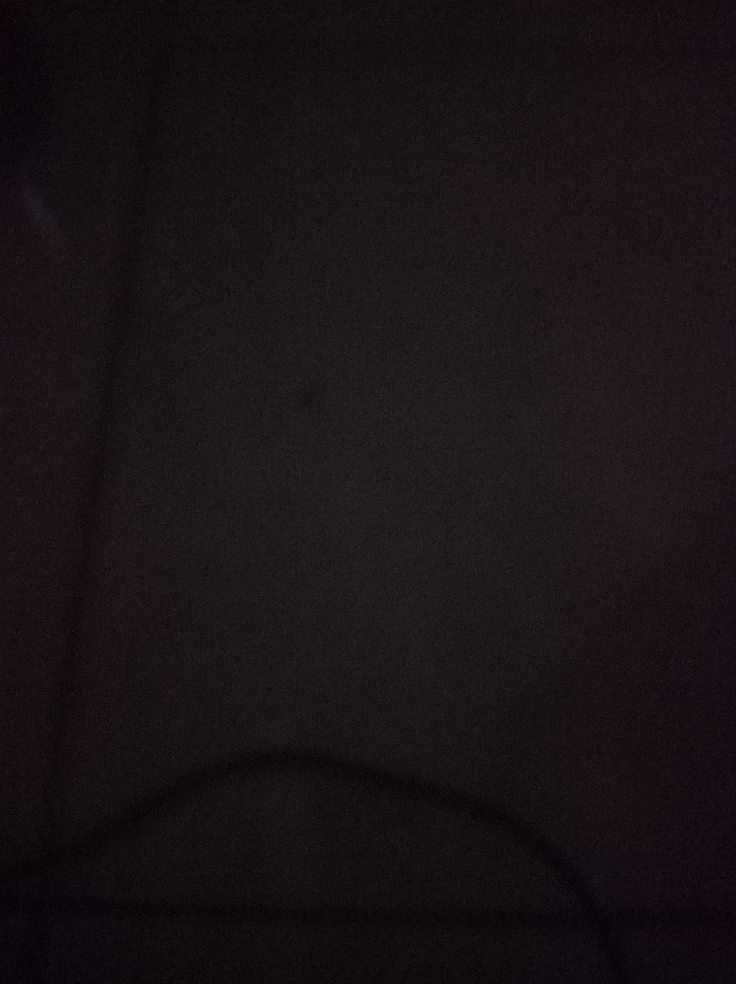 The image is a very dark, grainy photograph with low visibility. It appears to be an indoor setting, possibly a room or a dimly lit outdoor area. The dominant color is a deep, almost blackish brown, with subtle variations in shade suggesting the presence of a textured surface, perhaps fabric or a wall. There is a faint, curved line in the lower portion of the image, which could be a shadow, a fold in cloth, or a very dark object. No specific details about people, actions, or identifiable objects can be discerned due to the extreme darkness and poor image quality. The location in Tembung, Indonesia, cannot be determined from the visual information provided in the image.