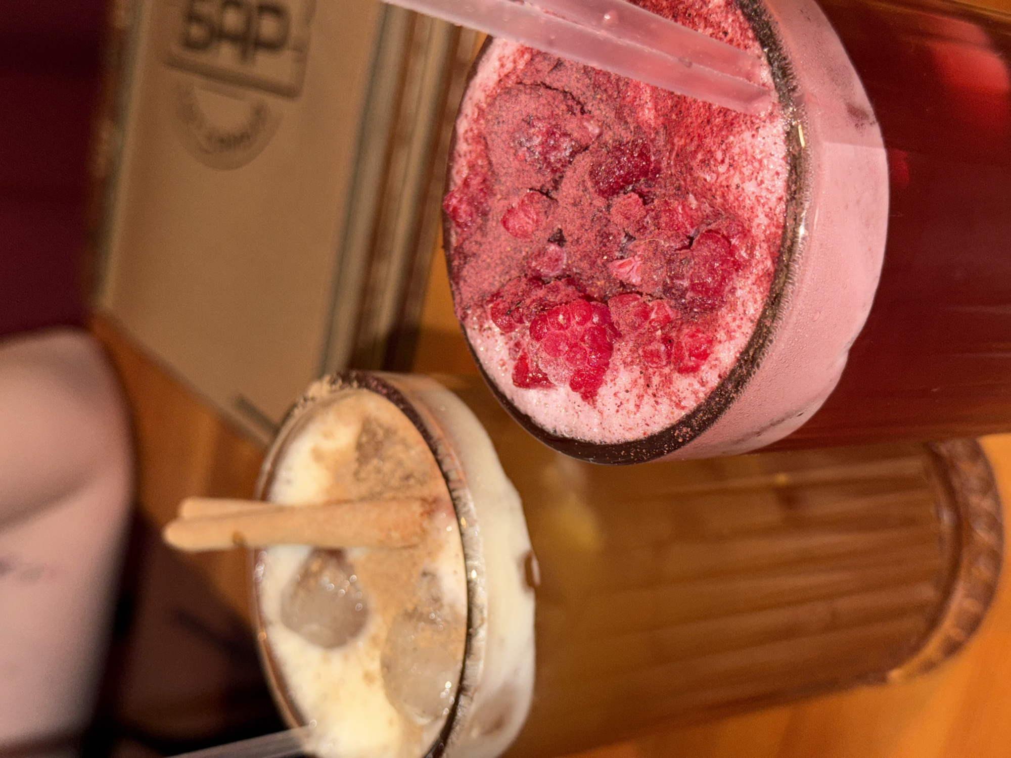 Two chilled drinks, one with raspberries and the other with ice and what appears to be cinnamon sticks, sit on a wooden surface beside a menu or book with the initials "SAP" on the cover. The location is Perm, Russia.