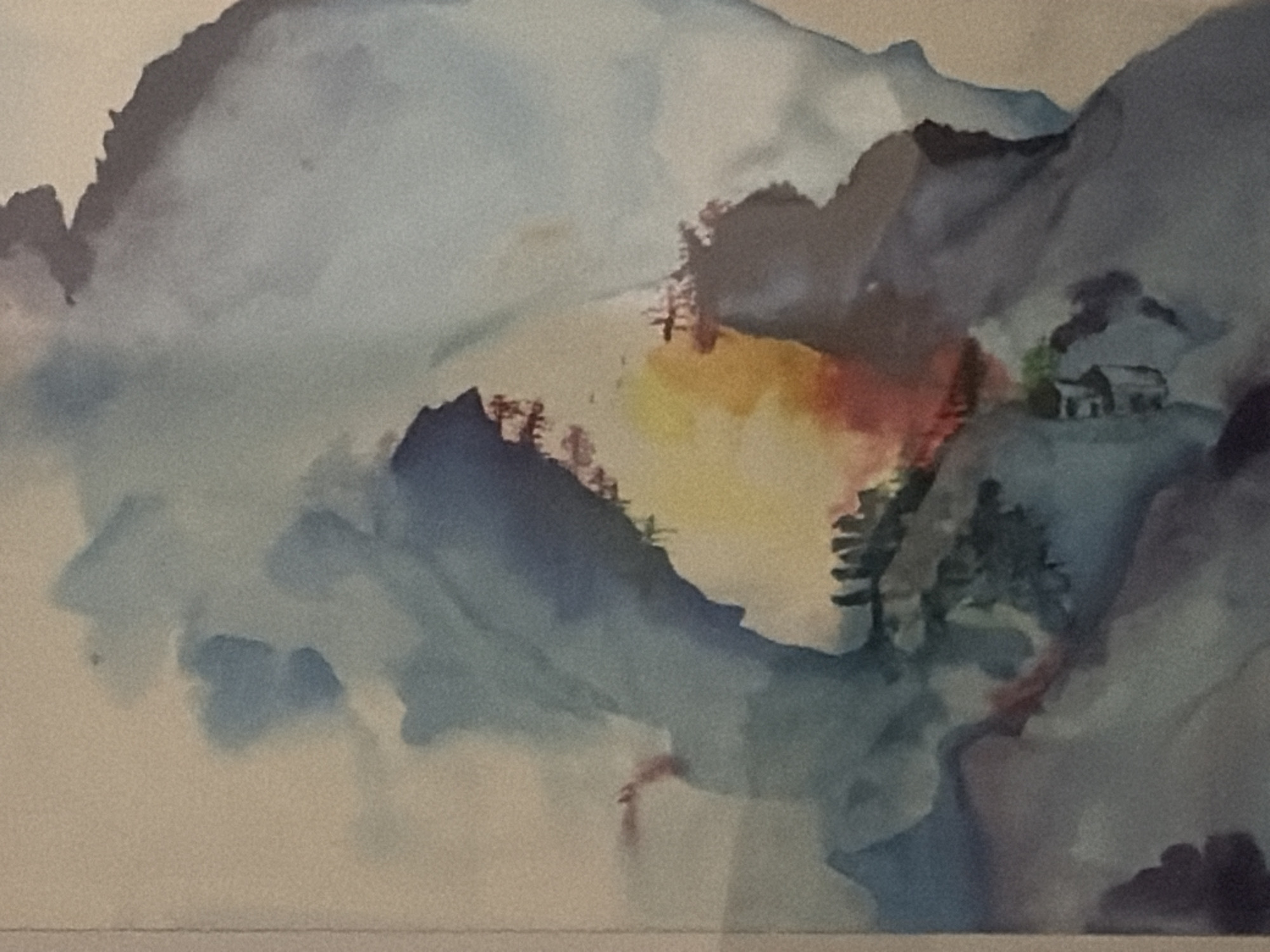 This is a watercolor painting depicting a misty mountain landscape. The scene features rolling blue and gray mountains shrouded in fog. In the middle ground, there is a clearing with a splash of yellow and red, suggesting a sunrise or sunset. Perched on a rocky outcrop in the upper right corner of the clearing are two small, simple buildings, possibly a house and a shed, with dark green trees surrounding them. The foreground is dominated by abstract washes of blue and gray, hinting at more mountains or clouds. The painting has a soft, ethereal quality due to the watercolor technique and the atmospheric depiction of the landscape.
Regarding the location in Germasogeia Municipality, Cyprus, this is a natural landscape painting and does not depict any specific identifiable landmarks or urban elements within the municipality. Therefore, it is impossible to pinpoint a specific location within Germasogeia based solely on this image.