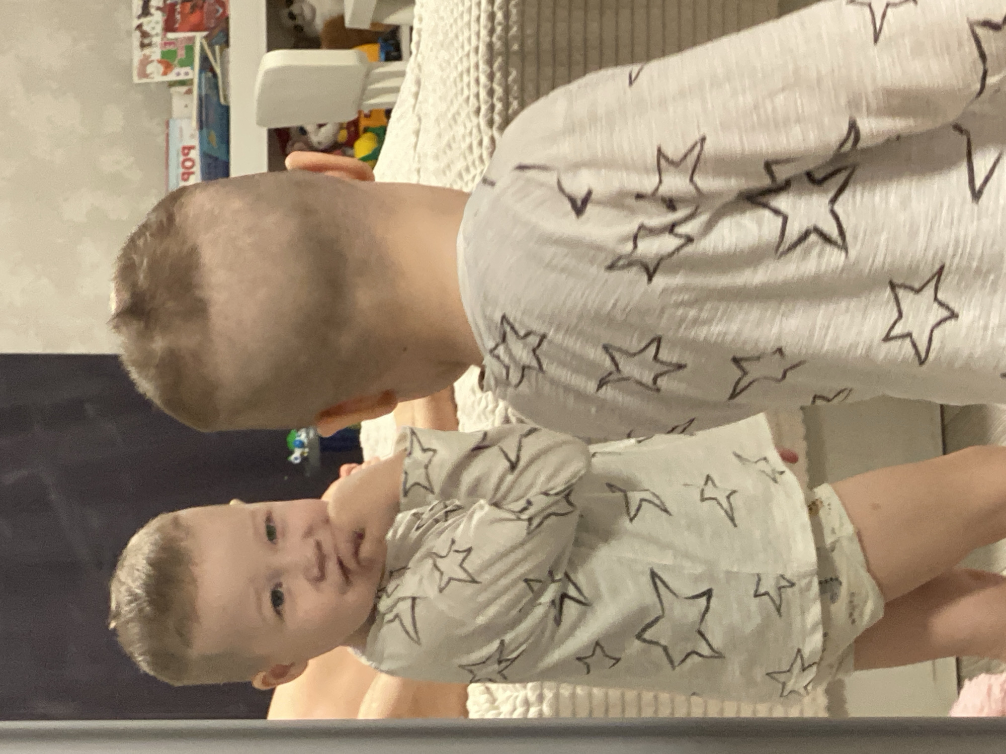 Two young children are present in the image. One child, appearing older, is facing away from the camera. The other child, presumably younger, is facing the camera. Both children are wearing clothing with a star pattern. The location is not discernible from the image. The city of Sochi, Russia, cannot be confirmed. There are no discernible actions or interactions taking place, and the environment is vaguely defined by a bed and some other objects.