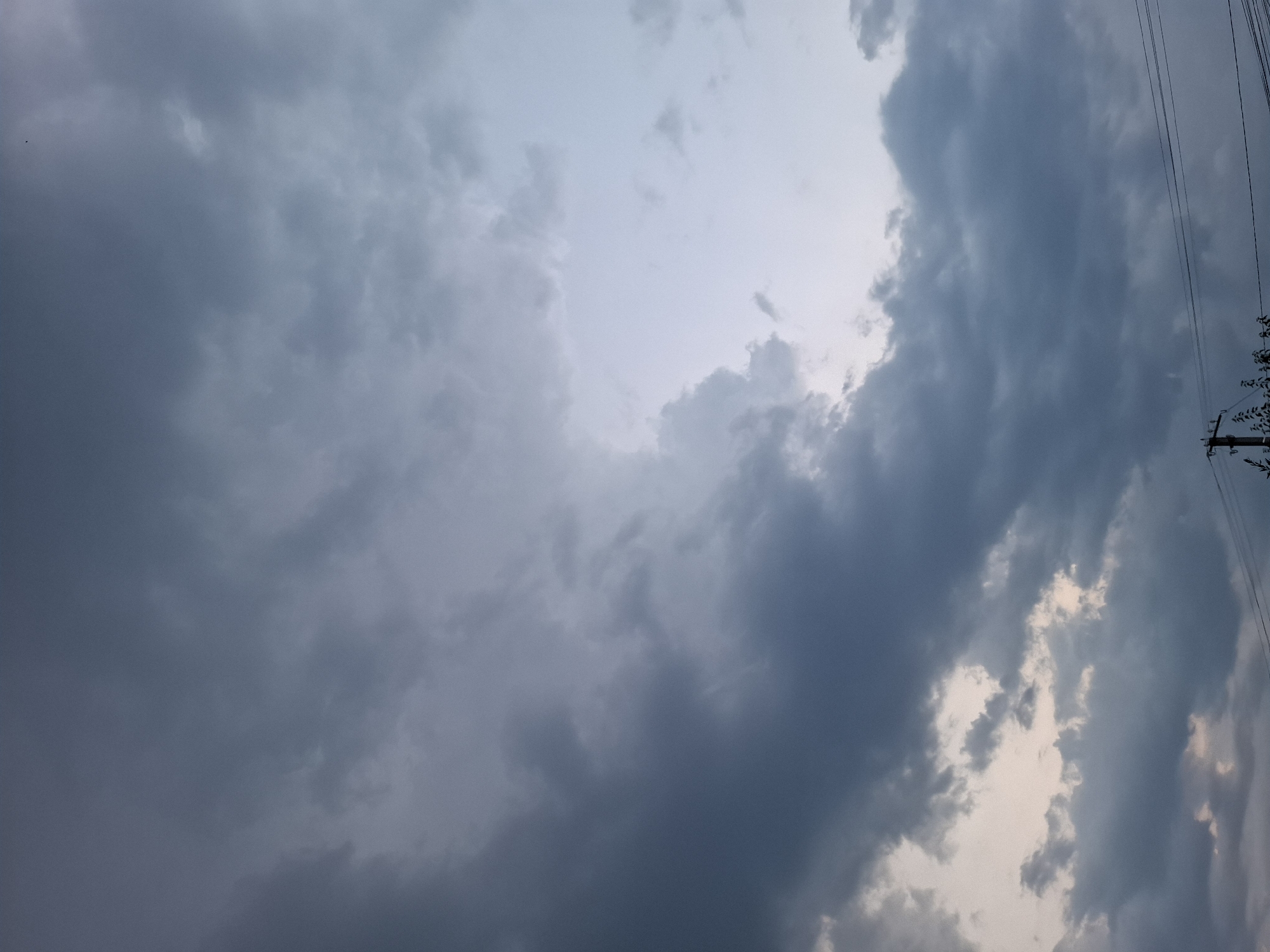 The image shows a cloudy sky over the village of Dubăsarii Vechi, Moldova. The clouds are dark and heavy, suggesting an approaching storm. The sky is a mix of dark grays and lighter blues, with some breaks in the clouds revealing a lighter sky. In the foreground, there are power lines and a utility pole. The overall impression is one of an overcast and potentially stormy day.
