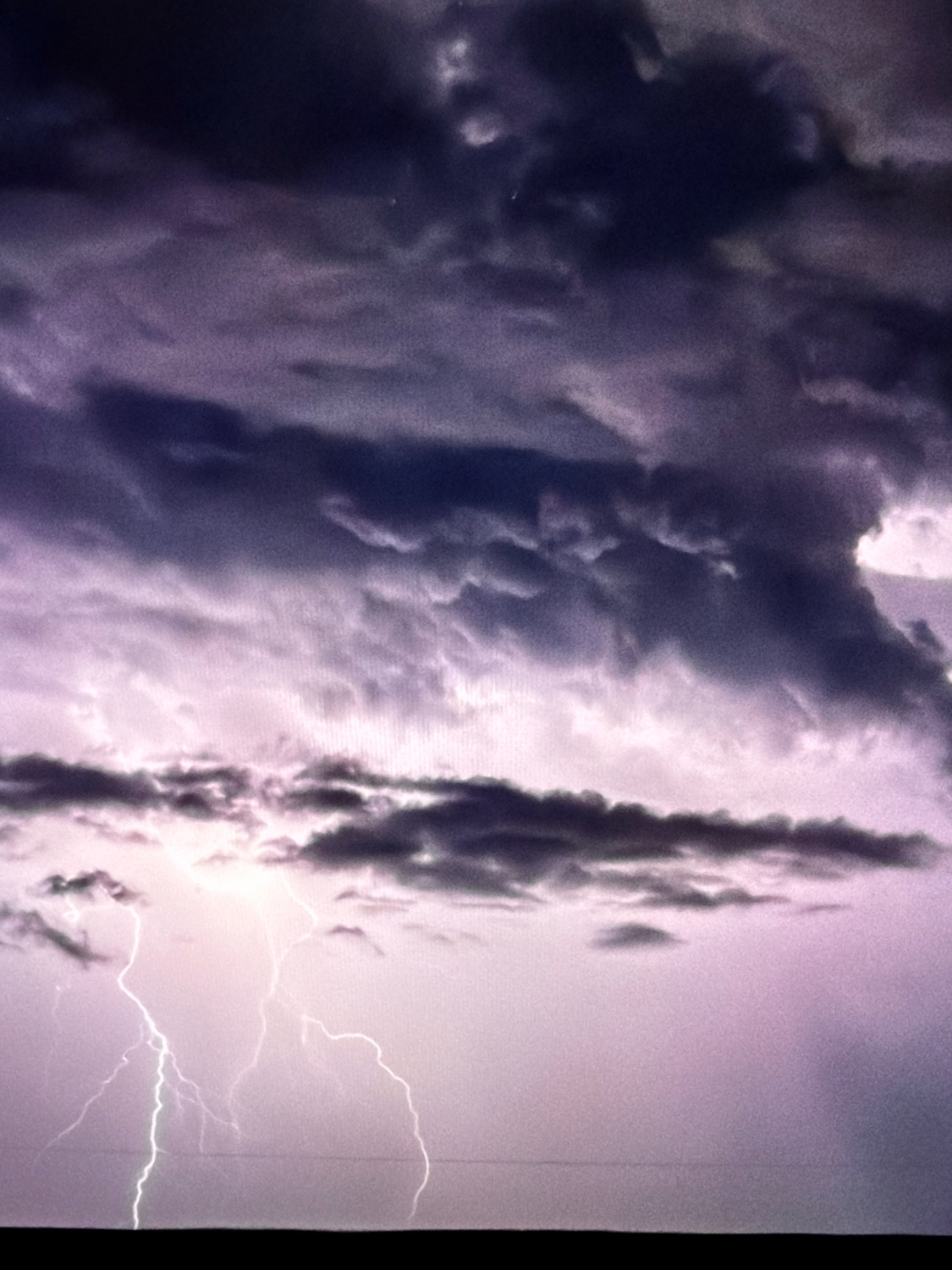 The image depicts a dramatic sky filled with dark, ominous storm clouds. Several bolts of lightning illuminate the scene, striking downwards from the clouds. The ground below is a dark, silhouetted band, suggesting a flat, possibly rural landscape. The overall impression is one of a powerful and active thunderstorm. There are no visible people, structures, or distinct landmarks that would specifically identify the location as Kafr Yasif, Israel.