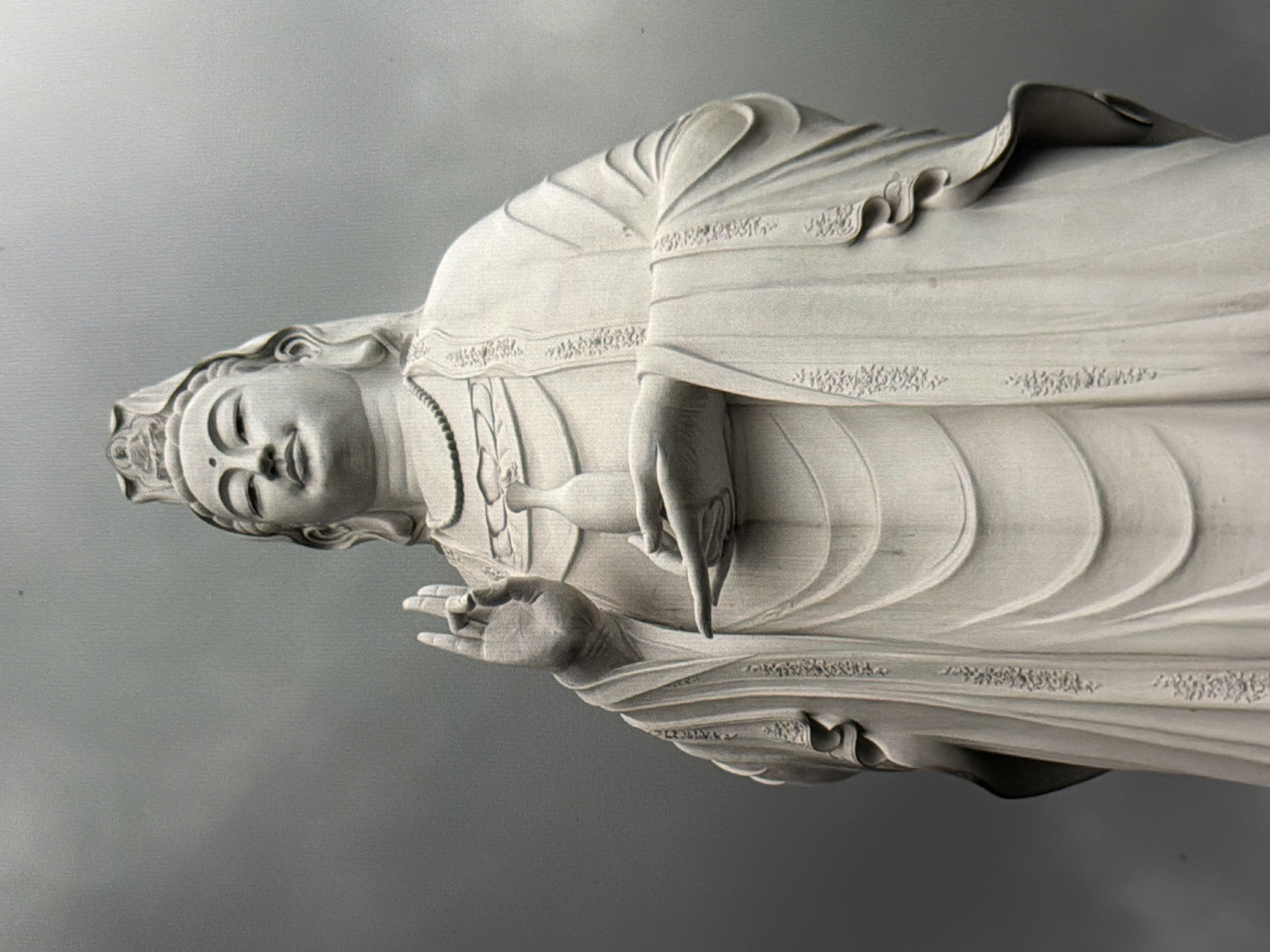A detailed statue of the bodhisattva Avalokiteśvara, often associated with mercy and compassion, is depicted. It is a white, intricately carved sculpture of a human figure with draped clothing and a serene face. The statue is located within the city of Đà Nẵng, Vietnam.