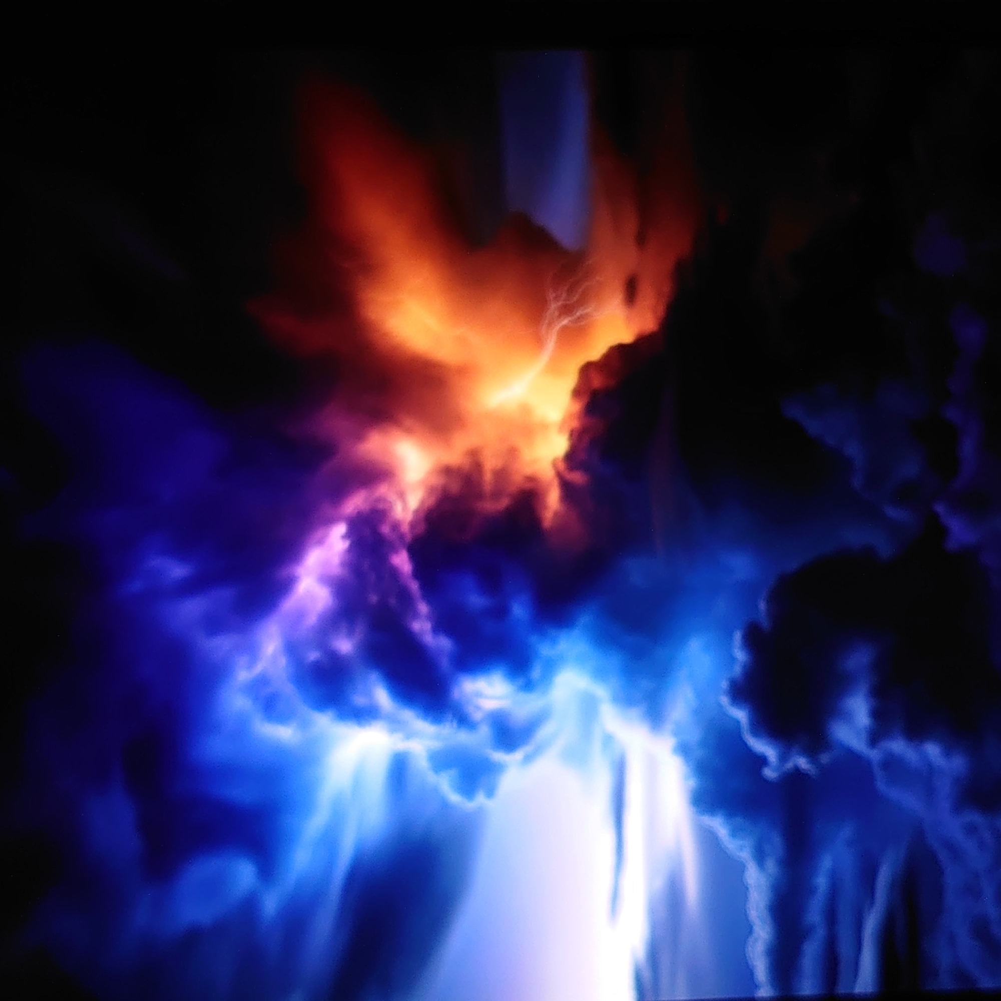 This is a digital image depicting a dramatic and abstract phenomenon that resembles a celestial or cosmic event. The scene is dominated by swirling masses of light and color against a dark background.
The subjects appear to be abstract forms of light and energy, possibly representing a nebula, a volcanic eruption, or a powerful atmospheric disturbance. There are no discernible people or man-made objects. The setting is entirely abstract, evoking a sense of immense scale and power, possibly a cosmic void or a stylized representation of a natural event.
The activity taking place is suggested by the dynamic interplay of colors and forms. Intense orange and yellow hues erupt from the upper central area, contrasting sharply with deep blues and purples that swirl and descend from the sides and lower portion of the image. Streaks of white light, reminiscent of lightning or intense energy beams, are visible within the darker blue formations, particularly in the lower half of the frame. The overall impression is one of explosive energy, turbulent forces, and possibly creation or destruction on a grand scale.
Notable details include the stark contrast between the bright, fiery colors and the deep, dark background. The texture of the light and energy is rendered in soft, painterly strokes, giving the image a dreamlike or otherworldly quality. The light appears to be emanating from within the forms, suggesting an internal source of power. There are no clear indicators of time of day, weather, or specific location cues, beyond the abstract and potentially violent nature of the depicted event. The emotions evoked are awe, wonder, and perhaps a sense of the sublime or even fear due to the intense and chaotic display of energy.
There is no visible text within the image. The location context of Belorechensk, Russia, does not appear to be visually represented or suggested by any elements within the image itself.