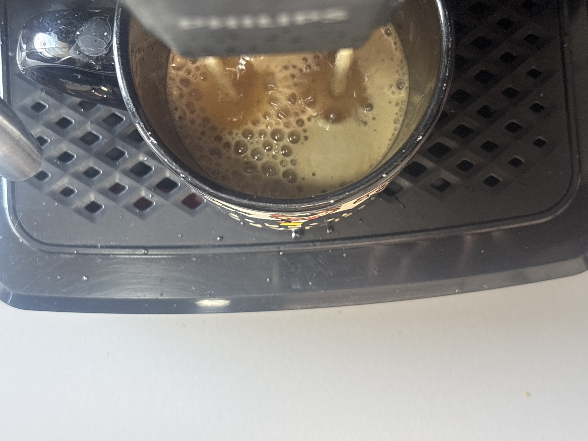 A close-up, top-down view shows a coffee mug filled with coffee being brewed by a Philips coffee maker. The mug sits on the coffee maker's drip tray, characterized by a black, diamond-patterned grid. The surrounding environment appears to be a white countertop. The location in the city of Buenavista, Mexico, is not visible in the image.