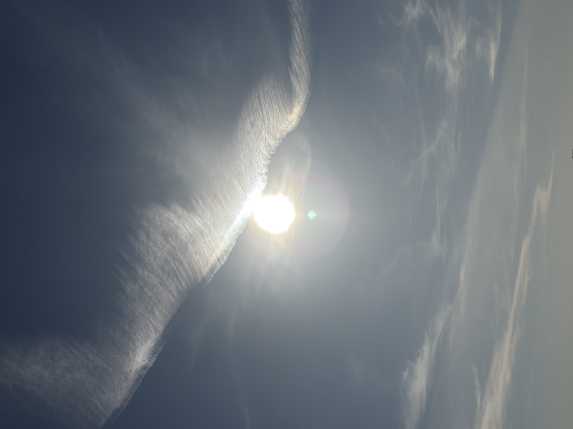 The image shows a daytime sky with the sun obscured by a wispy, striated cloud formation. Other less dense clouds are visible in the periphery. The location (Votkinsk, Russia) is not evident from the visual information in the image. There are no people or identifiable objects in the image. The environment is the sky.