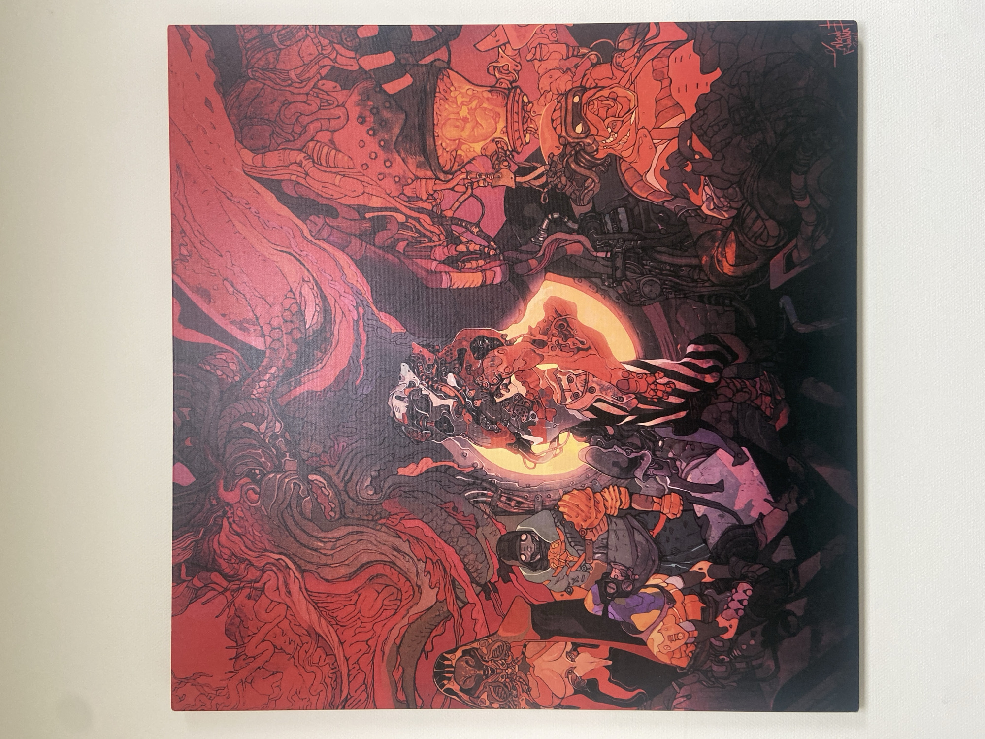 The image shows the cover of a vinyl record with a vibrant, intricate illustration in shades of red, orange, and black. The artwork depicts a chaotic, fantastical scene with biomechanical elements and figures. In the center, a person wearing a helmet and goggles, and dressed in a grey and orange outfit, appears to be operating some machinery. To their left, a large, organic, red form dominates, with complex, almost root-like structures. Above and around the central figure, there are various mechanical components, wires, tubes, and what looks like a glowing, biological-looking orb.
Towards the bottom of the cover, there are other figures, some of which appear to be in a more skeletal or biomechanical form. The overall impression is one of a dark, futuristic, or perhaps dystopian setting, filled with action and a sense of intense, possibly dangerous, activity. The style is highly detailed and somewhat grotesque, with influences from science fiction and fantasy art.
In the upper right corner of the cover, there is a small area of text, likely a signature or artist's mark, written in what appears to be East Asian script. The image itself is a flat, straight-on shot of the record cover against a plain white background.