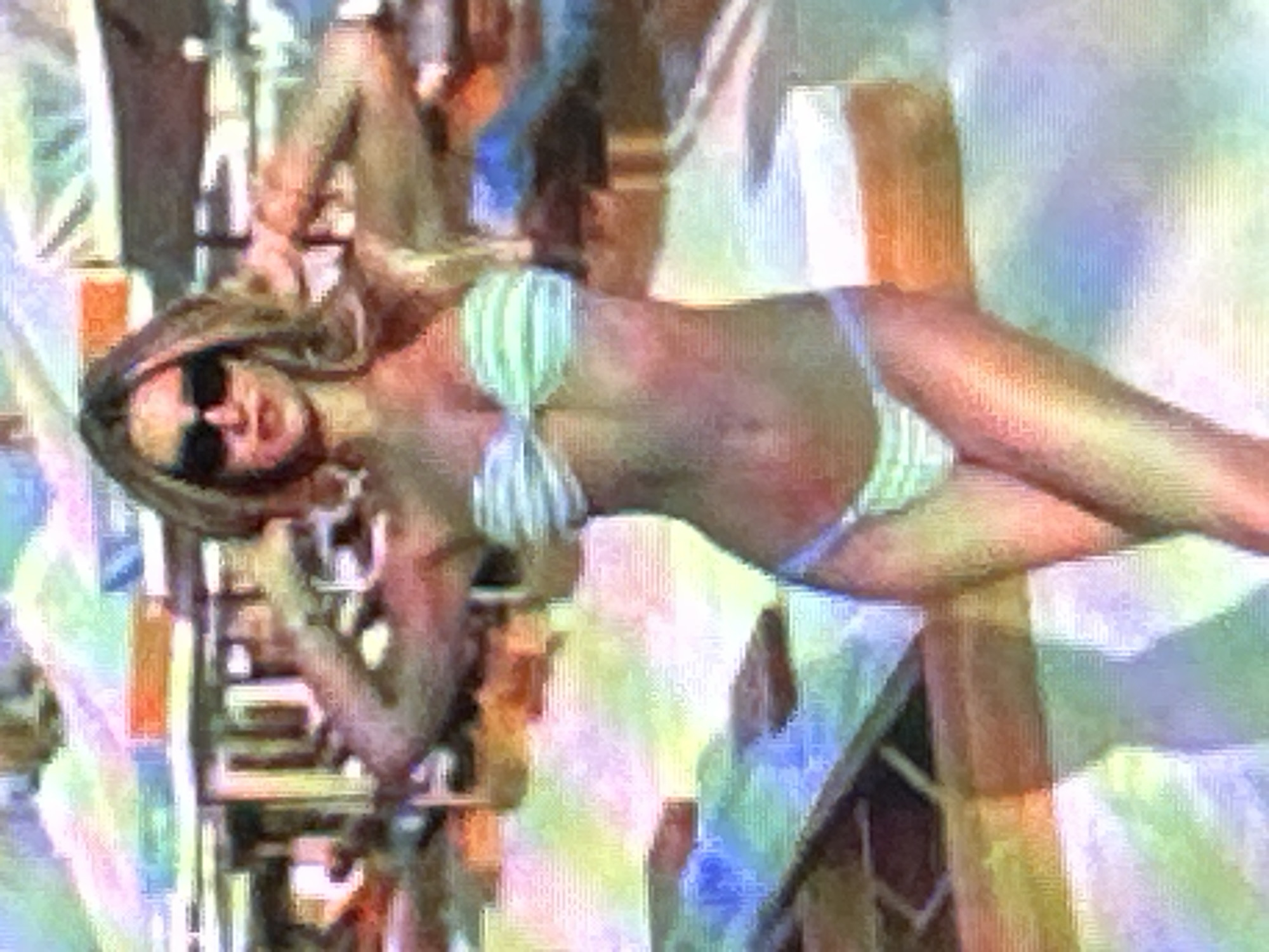 The image shows a woman wearing a striped bikini and sunglasses. She is standing in front of a blurry background that appears to be an outdoor setting with some structures and colorful elements, possibly a beach or poolside area. Her arms are raised, and she is looking towards the camera. The image quality is low, with visible pixelation and color distortion. There is no information available to determine the location within the city of Sofia, Bulgaria.