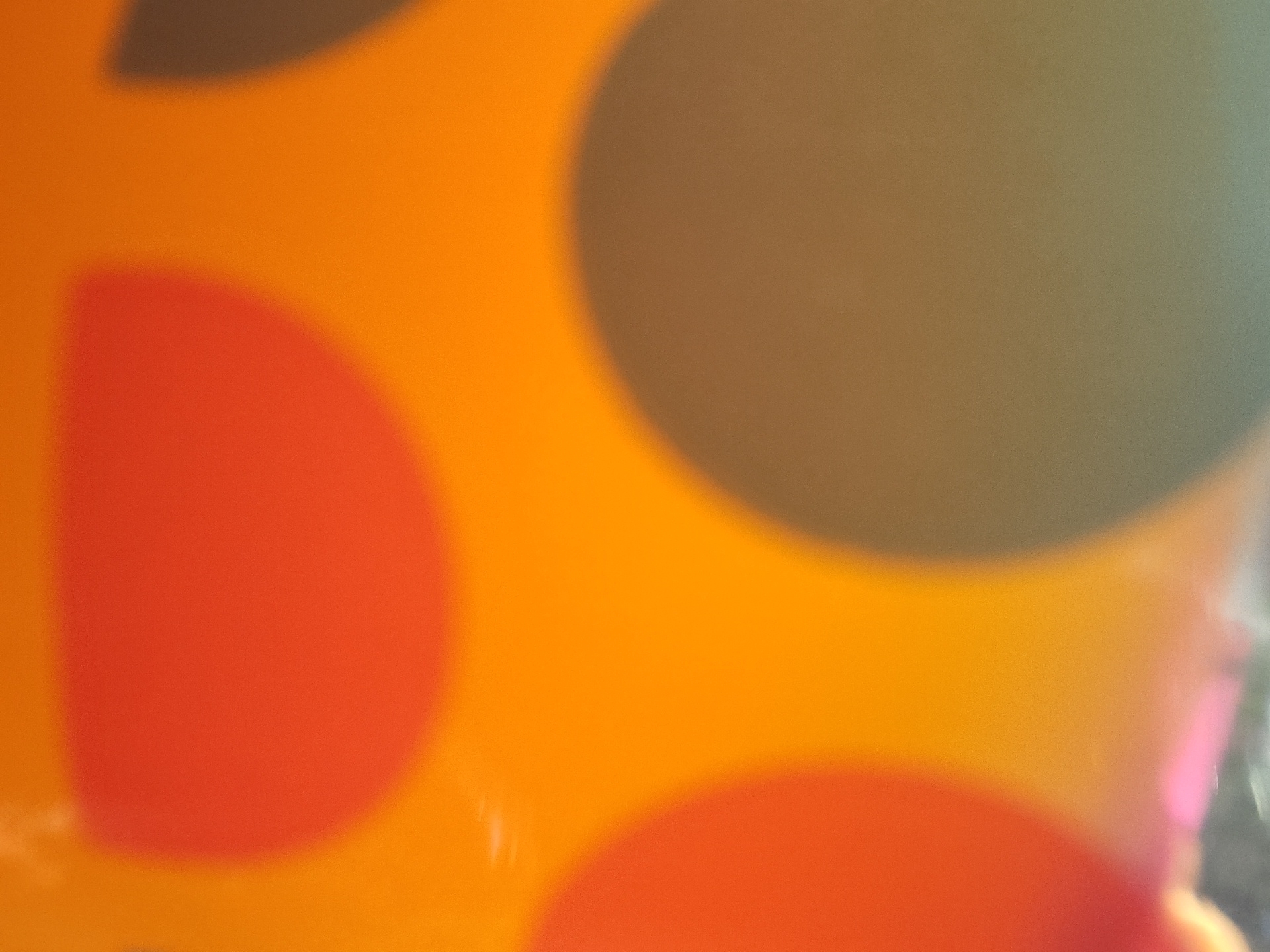 This image is an abstract, close-up photograph of a surface with large, blurred polka dots in shades of orange, red, and a muted green-brown. The overall impression is soft and slightly grainy due to the focus and lighting. There is no discernible context for the location within Vlasatitsa, Bulgaria, or any people, objects, actions, interactions, or environmental elements that would suggest a specific scene.