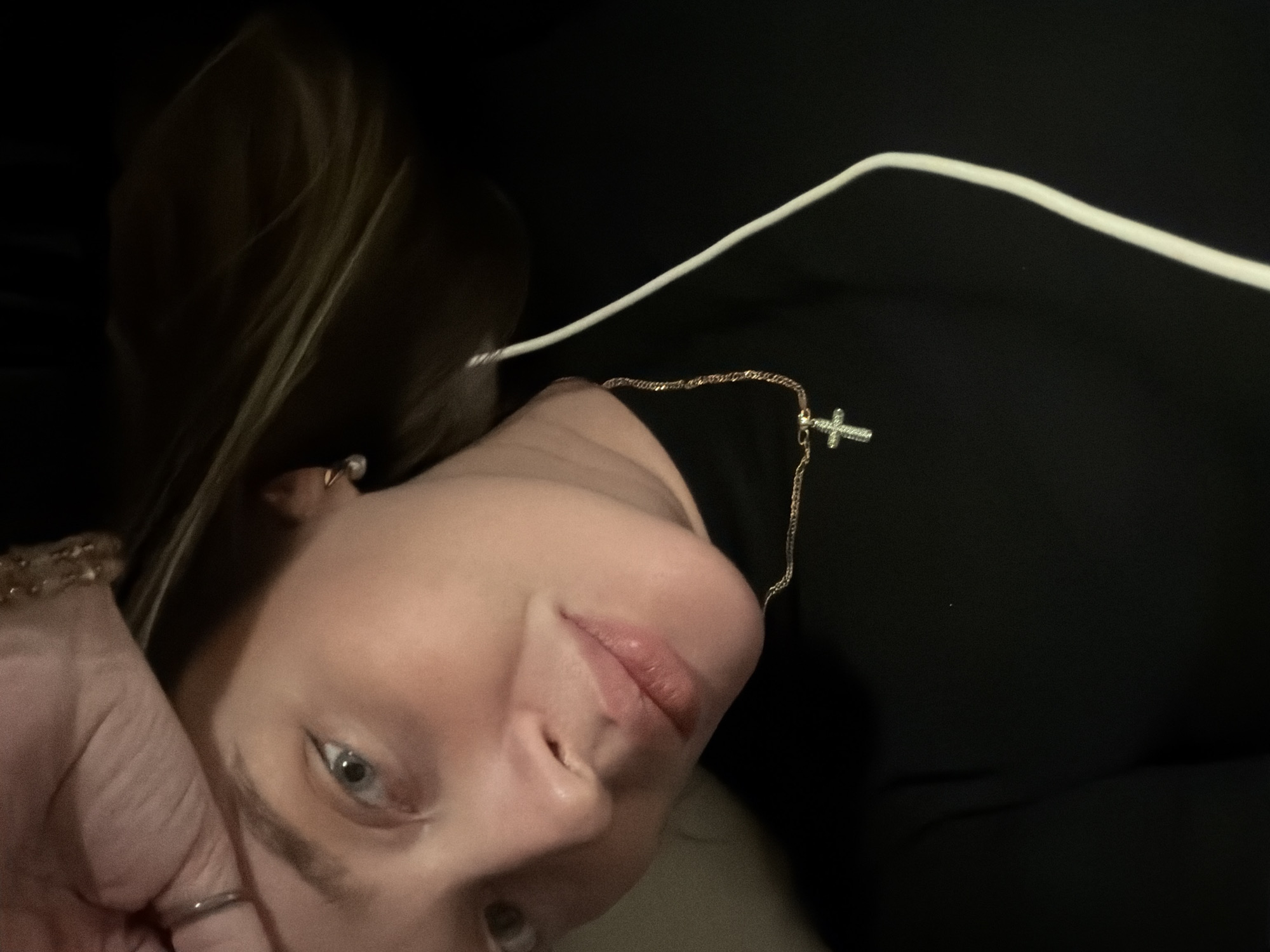 A photograph presents a close-up, tilted portrait of a person with fair skin, light-colored eyes, and blonde hair. The person is wearing a black top and a gold necklace with a cross pendant. A white cable is partially visible above their shoulder. The individual's face is positioned in the lower-left quadrant, and their hand is visible in the lower-left corner. There is no discernible information that places the scene in Moscow, Russia.