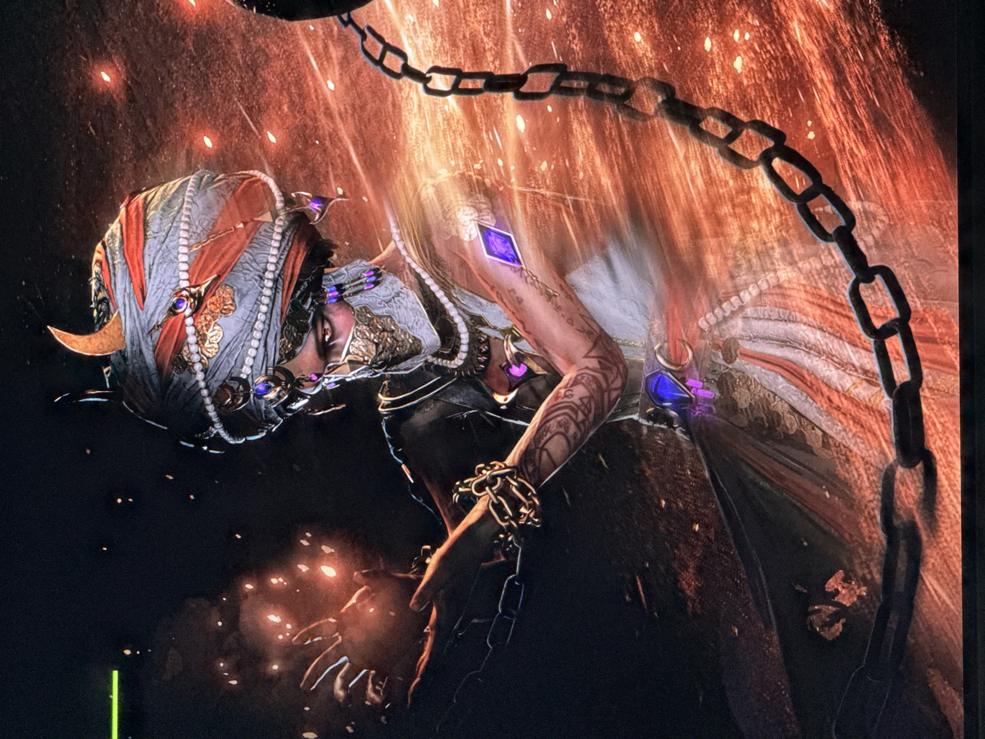 This dynamic digital artwork depicts a stylized, human-like figure, possibly female, amidst an intense, fiery background. The central subject is adorned in elaborate, dark attire with rich golden and metallic accents, intricate patterns, and pearl strands draped around her neck and shoulders. She wears a turban-like headpiece featuring similar gold ornamentation, pearls, and a crescent-shaped element above her left eye. Distinctive purple, glowing, diamond-shaped gems are visible on her arm and various points of her clothing. Her right arm, covered in intricate tattoos, has one such gem embedded.
A prominent black metal chain runs diagonally across the upper portion of the image, with another section wrapped tightly around the figure's left wrist, suggesting themes of power, struggle, or entanglement. The figure is positioned dynamically, as if caught in a powerful current or performing an action. Her face, partially obscured by shadow and ornaments, conveys an intense or focused expression.
The background is a vibrant burst of orange and red light, characterized by vertical streaks and scattered glowing particles or embers, creating an impression of immense energy, magic, or an explosion. The overall atmosphere is dramatic and fantastical. A distinct, bright green vertical line is visible at the bottom left corner, appearing to be a screen artifact rather than part of the artwork. No text is visible within the image. While the image was provided in the context of Riga, Latvia, the depicted scene is a fantasy illustration rather than a direct representation of that location.