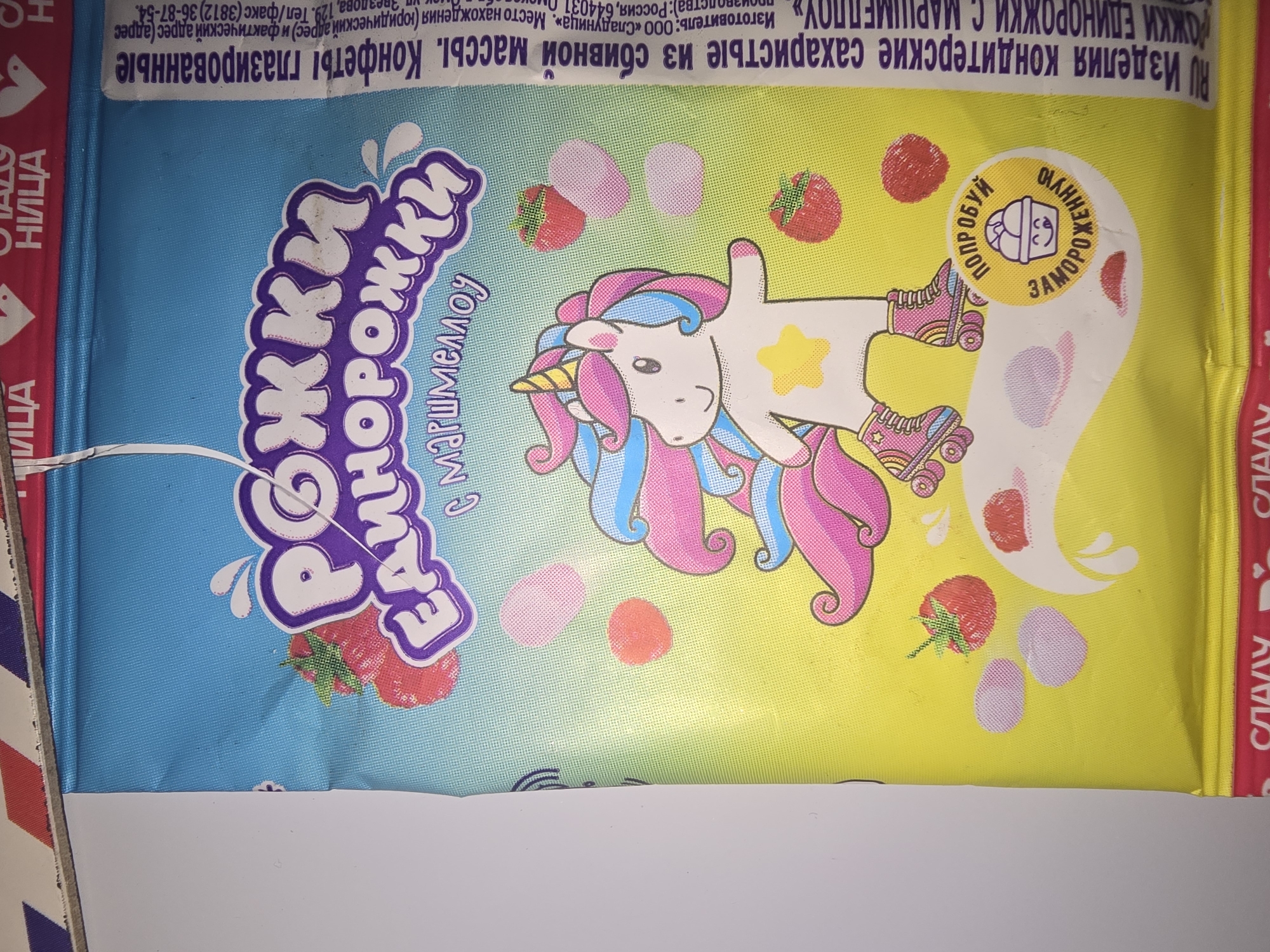 The image shows the packaging of a confectionery product. The packaging features a cartoon illustration of a unicorn wearing roller skates, surrounded by strawberries and marshmallow-like shapes. The product name "РОЖКИ ЕДИНОРОЖКИ" (Unicorn Horns) is prominently displayed in a stylized font, with "с маршмеллоу" (with marshmallow) below it. To the right of the illustration, there is text in Russian indicating the product is "Изделия кондитерские сахаристые из сбивной массы. Конфеты глазированные" (Confectionery products, airy sugary from whipped mass. Glazed candies). There is also an address and phone number for the manufacturer: "Изготовитель: ООО «Сладуница». Место нахождения (юридический адрес) и фактический адрес (адрес производства): Россия, 644031, г. Омск, ул. Звезда, 129. Тел/факс (3812) 36-87-54." This translates to "Manufacturer: Slavdnitsa LLC. Location (legal address) and actual address (production address): Russia, 644031, Omsk, Zvezda Street, 129. Tel/fax (3812) 36-87-54."
The text does not contain any information about the city of Ulan-Ude, Russia. The provided image is a product package and does not depict any specific location within Ulan-Ude or any other city.