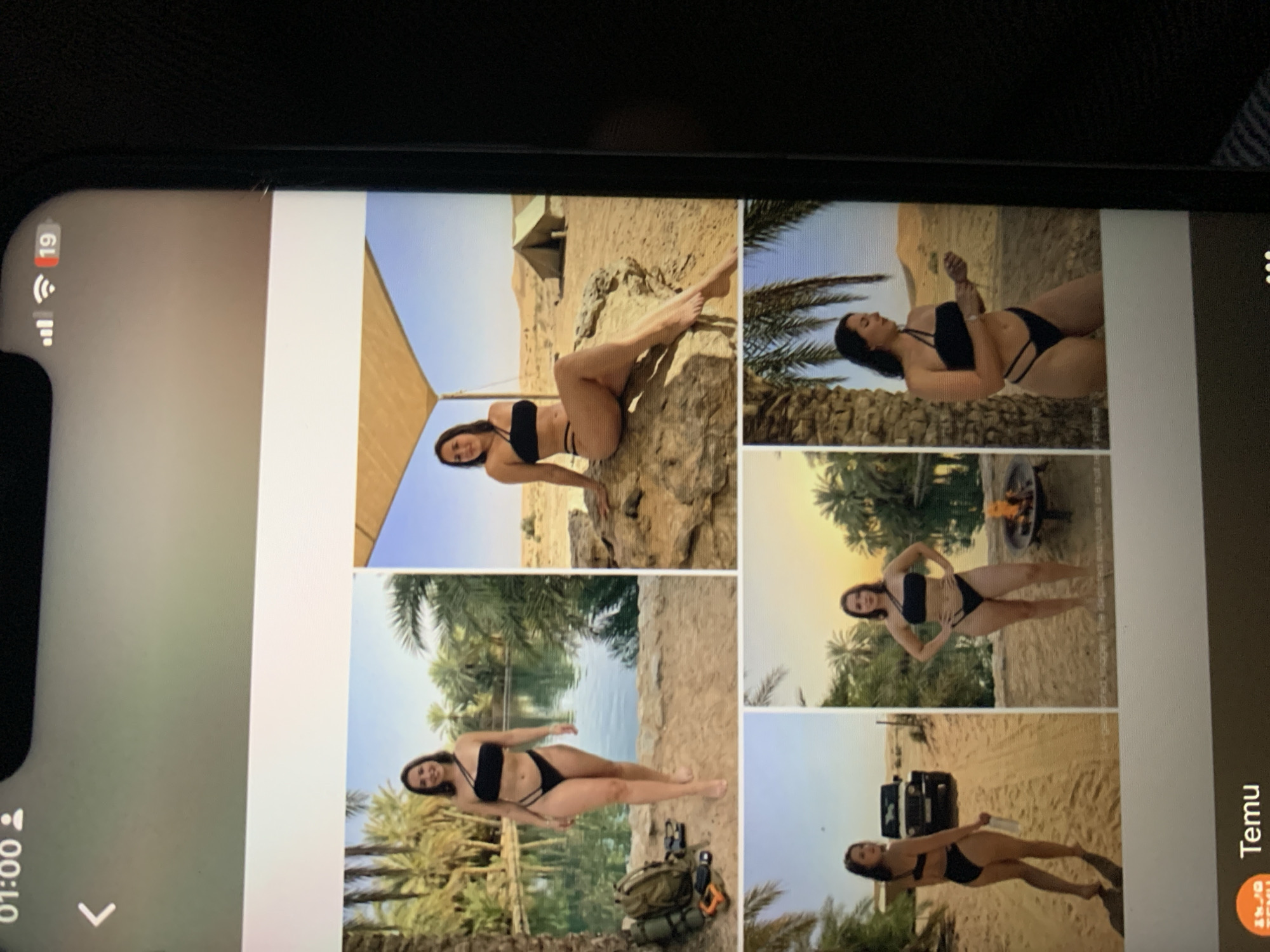 The image displays a collage of six photographs of a woman in a black bikini. The photographs are arranged in a grid of two rows and three columns. The woman is posing in various outdoor desert and oasis-like settings with palm trees.
The top row features:
1. The woman standing near a body of water surrounded by palm trees, with a backpack and camping gear on the sand.
2. The woman sitting on a large rock in a desert landscape with a tent in the background.
3. The woman posing on a rock in the desert.
The bottom row features:
4. The woman walking on a sandy path with a jeep in the background.
5. The woman standing in front of a campfire with palm trees and water behind her.
6. The woman standing in a desert landscape with palm trees.
The image also shows a phone screen interface at the top, with a clock displaying "01:00", a battery indicator, Wi-Fi signal, and a notification count of "19". At the bottom of the image, there is a section that appears to be from an app, with the Temu logo and name displayed, along with some dots which might indicate navigation or a carousel.
There is no visual information in the image that links it to the city of Zhmerynka, Ukraine.