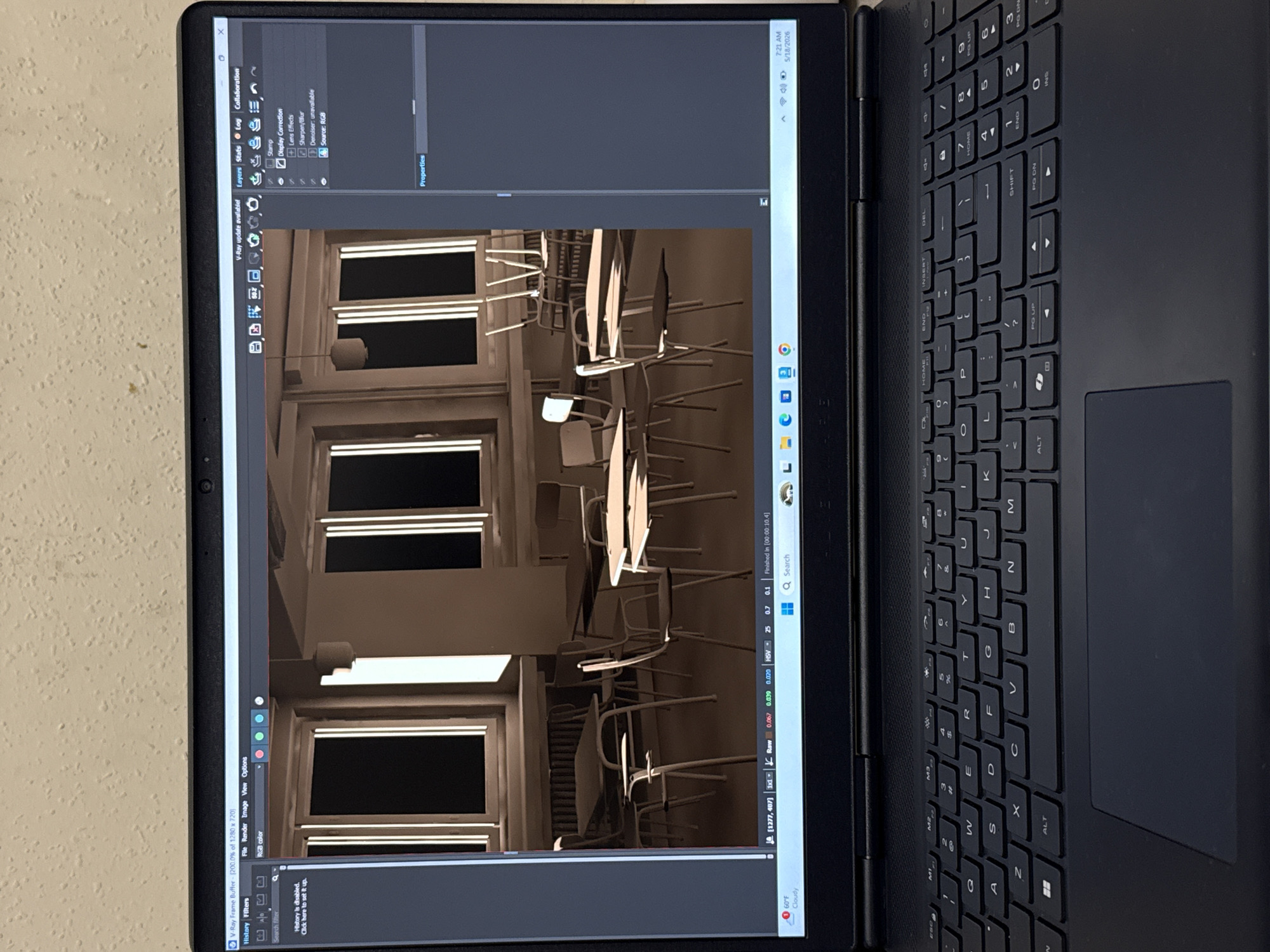A laptop is open, displaying a 3D rendering of a building interior, likely a classroom or office space with desks and chairs. The rendering is in sepia tones. The laptop keyboard is visible on the right side of the screen. The operating system interface shows a window titled "V-Ray Frame Buffer," indicating 3D rendering software is being used. The time on the laptop's status bar reads "7:21 AM" and the date is "5/18/2026." The laptop is resting on a light beige surface, possibly a table or desk. No individuals or actions are depicted in the photograph. The image offers no evidence to suggest this image relates to Yerevan, Armenia.