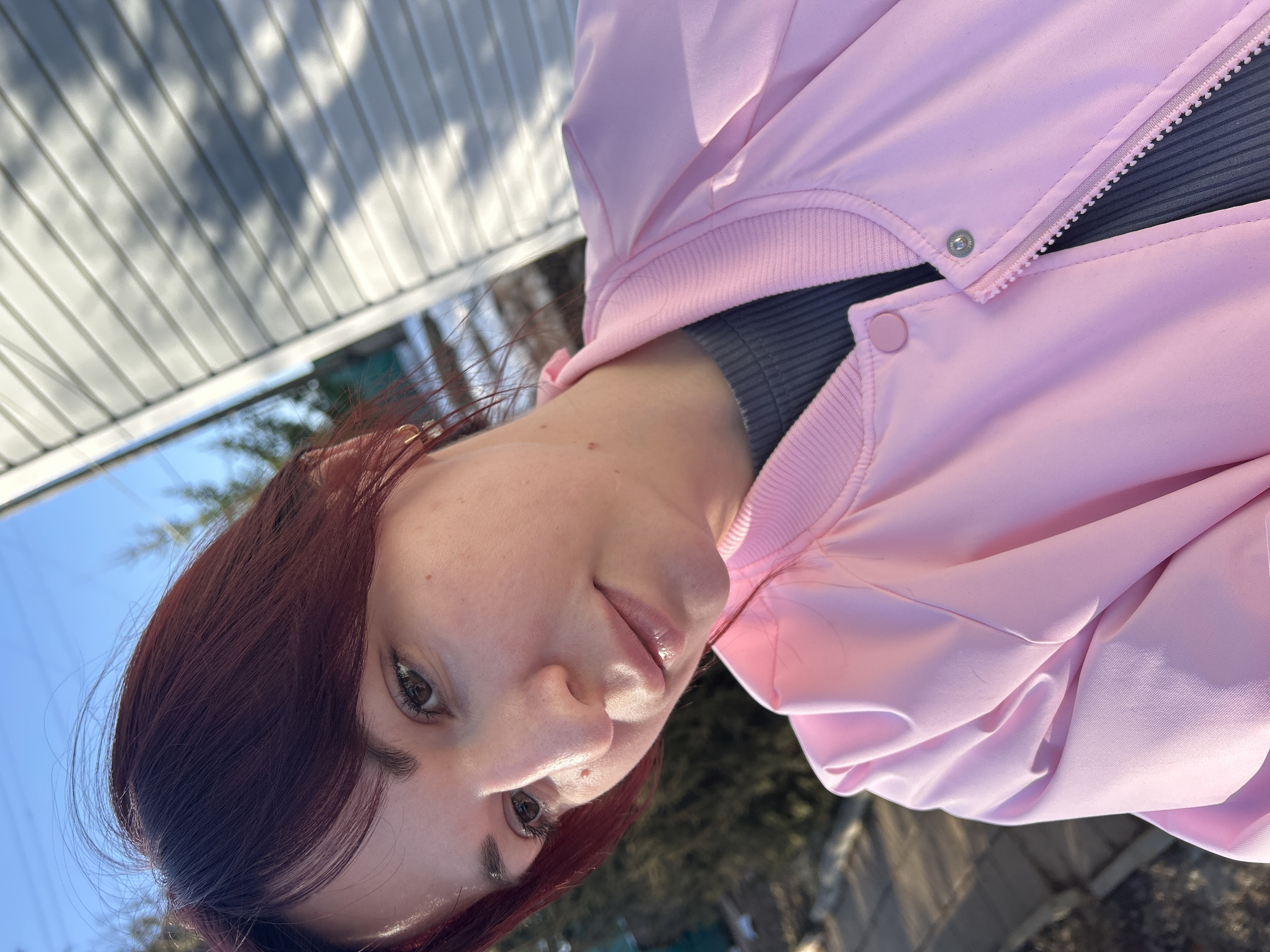 A photograph shows a woman wearing a pink jacket outdoors. The background indicates an urban environment. The image is taken at an angle, showing the woman's face and the surrounding scenery. There is no evidence to indicate a specific location within Фоки, Russia.
