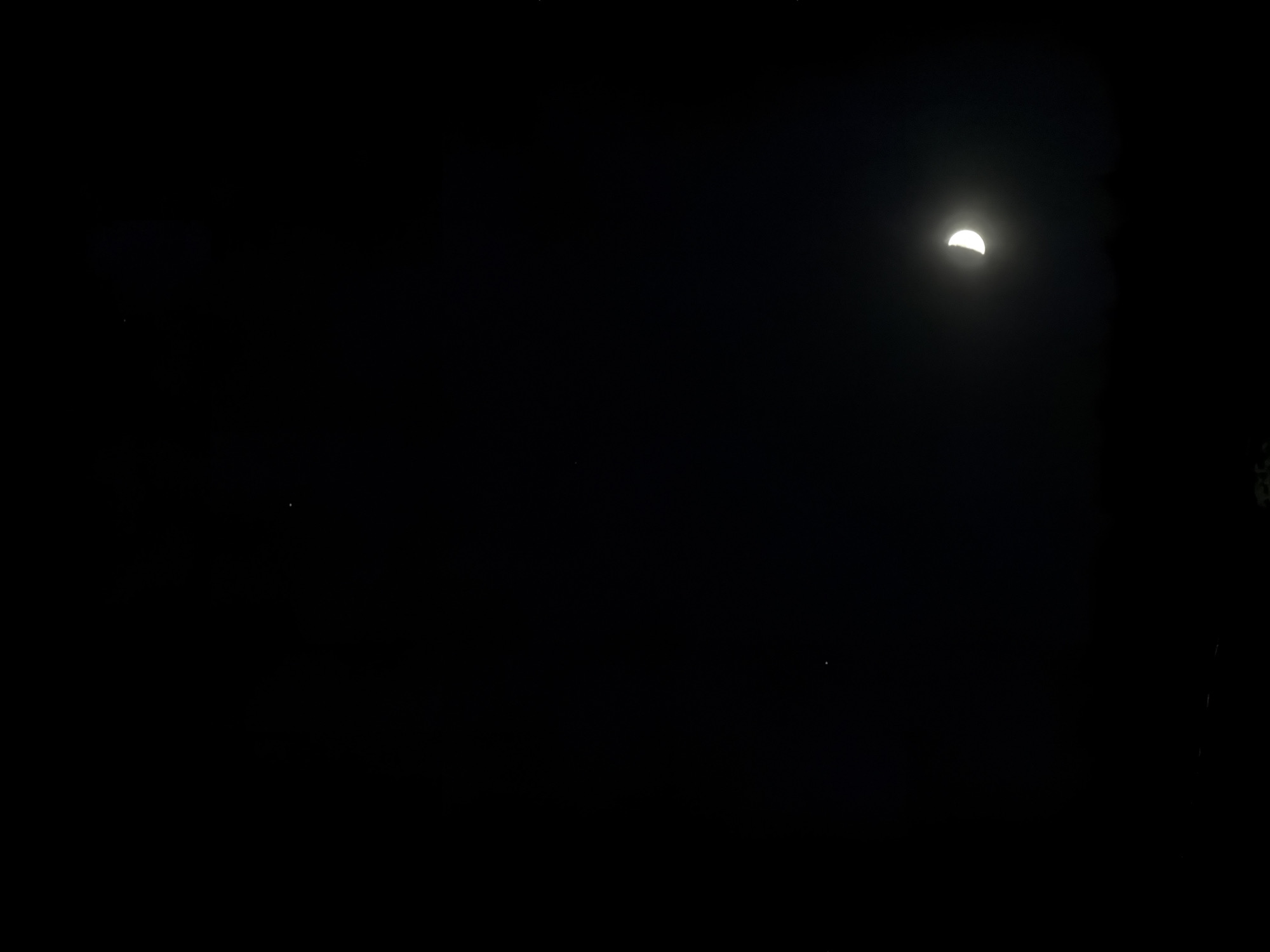 The image shows a dark night sky with a crescent moon in the upper right quadrant. A few faint stars are visible scattered across the dark background. There is no indication of the location being Izhevsk, Russia, or any presence of people, objects, actions, or interactions within the scene. The environment is limited to the night sky and celestial bodies.