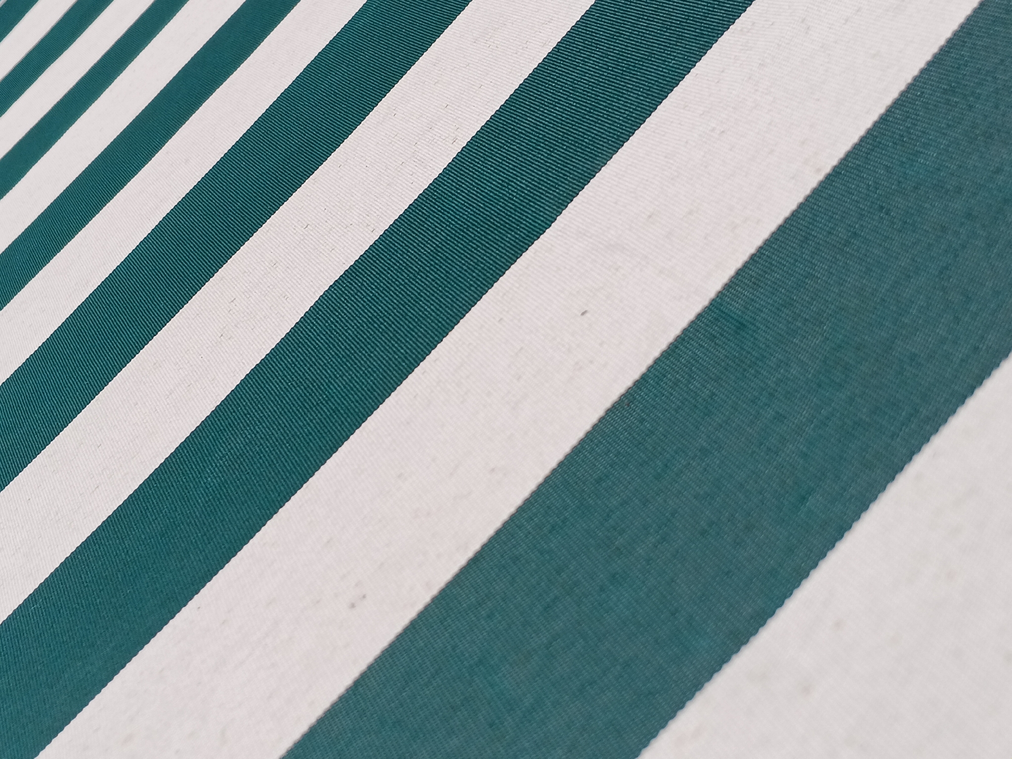The image shows a close-up view of a fabric with alternating white and teal stripes. The stripes run diagonally across the frame. The fabric has a visible woven texture.