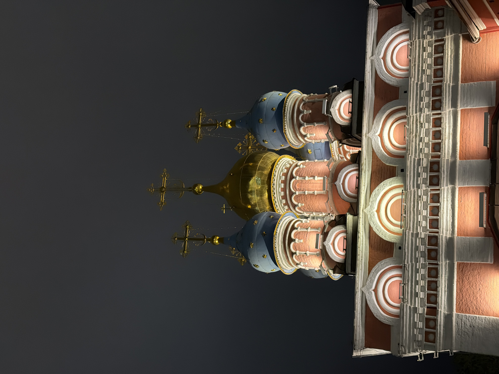 The image shows St. Basil's Cathedral in Moscow, Russia, at night. The colorful domes, crosses, and architecture of the cathedral are illuminated against the dark sky.