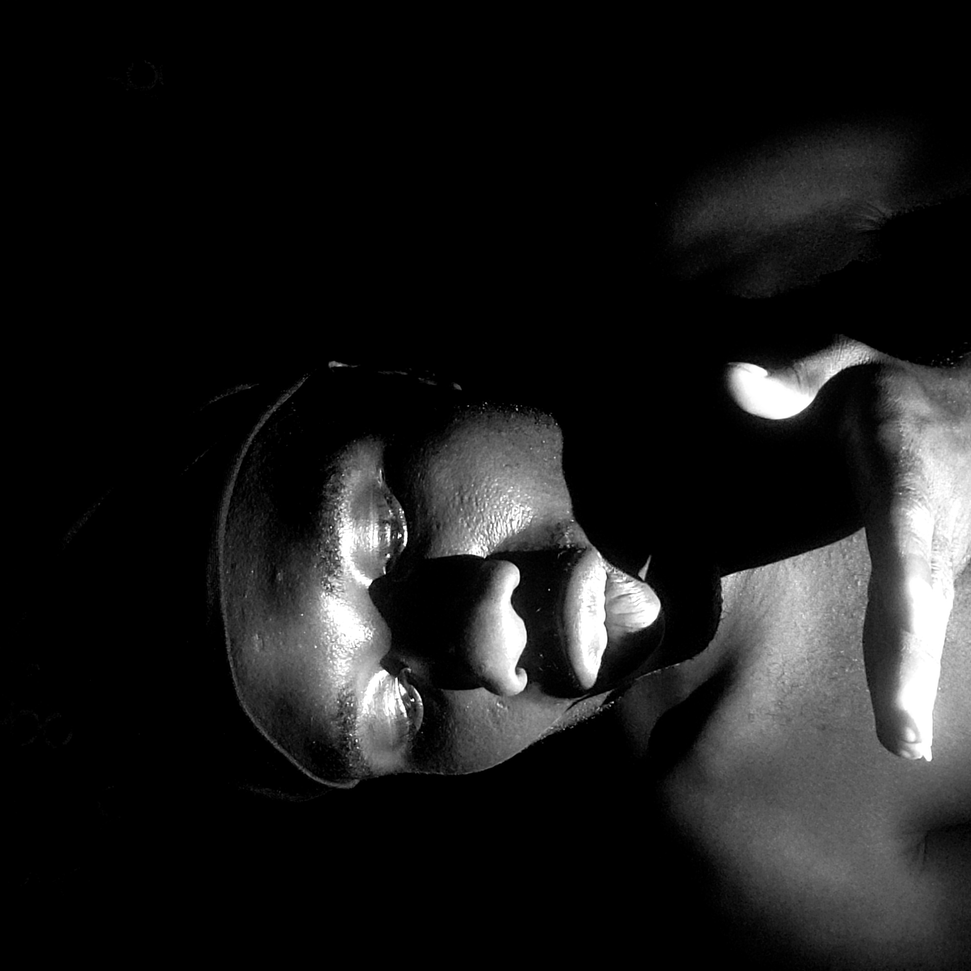 A close-up black and white photo depicts a person lying down with their face partially illuminated. A hand is positioned near the face, casting a shadow. The setting is undefined and there is no information suggesting a specific location in Narayi, Nigeria.