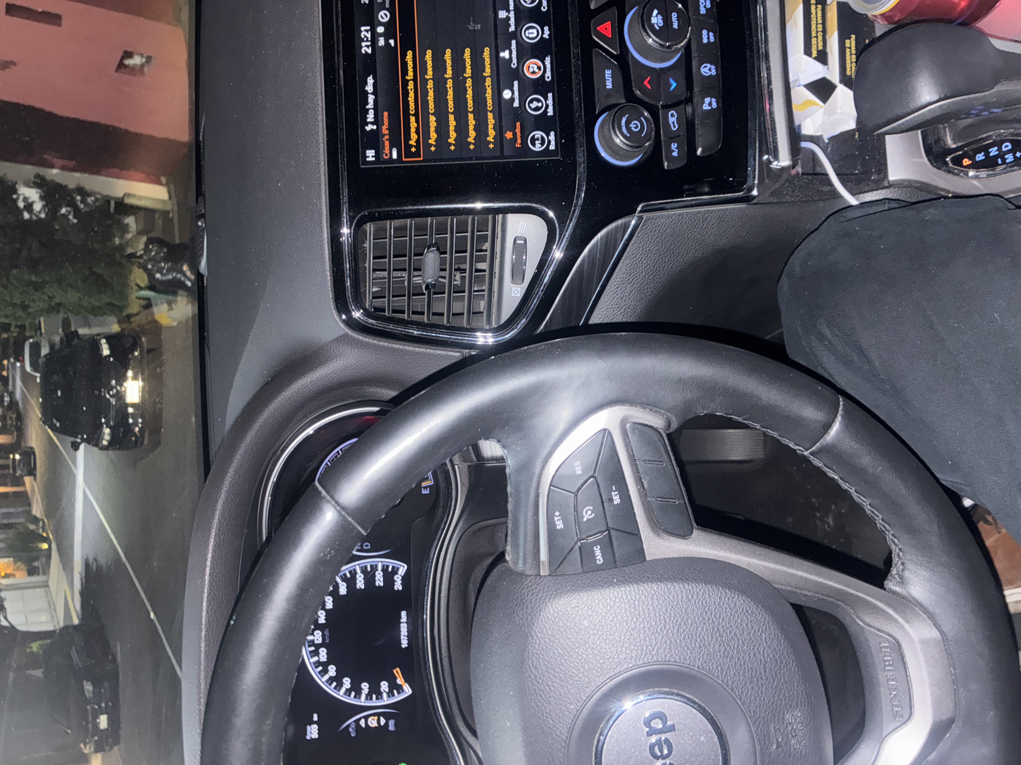 The image shows the interior of a Jeep, specifically the steering wheel, dashboard, and center console. The dashboard screen displays an interface in Spanish, prompting the user to "Agregar contacto favorito" (add favorite contact). The time is 21:21, and the phone is identified as "César's iPhone." The car's odometer reads 167363 km. The gear shift is set to park "P," with options for reverse "R," neutral "N," and drive "D." The driver is wearing black clothing. Through the windshield, a city street is visible. The image does not contain sufficient information to determine the location in Mexico City.
