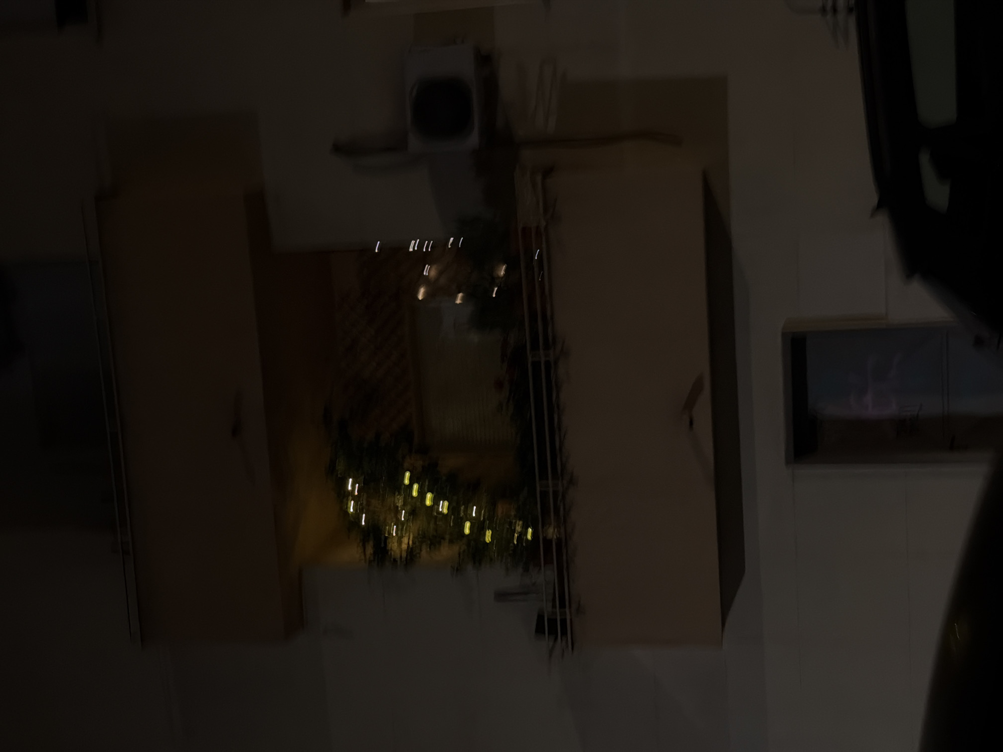 A blurred, poorly lit, overhead shot depicting the interior of a room, possibly in Vracar Urban Municipality, Serbia. Two light-colored, possibly wooden cabinets are visible. One cabinet is oriented vertically on the left side of the image, and the other is oriented vertically on the right side of the image. In between the two cabinets, a trellis-like wall with lights appears. In the top center of the image, there is a small white object, possibly an appliance. A part of a vehicle is on the right side of the image.