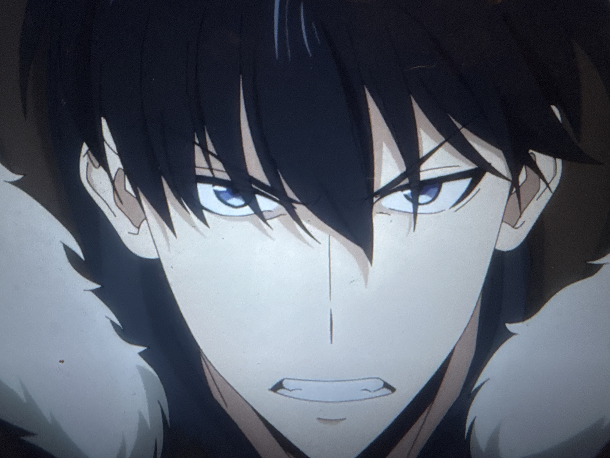 A close-up shot depicts a male anime character with dark hair and light blue eyes. He has a stern expression, with a furrowed brow and a slight clench to his jaw. He appears to be wearing a dark garment with a white, furry collar. The character's face is pale, with subtle shading to indicate facial structure. There is no indication of the city of London, United Kingdom in the image.