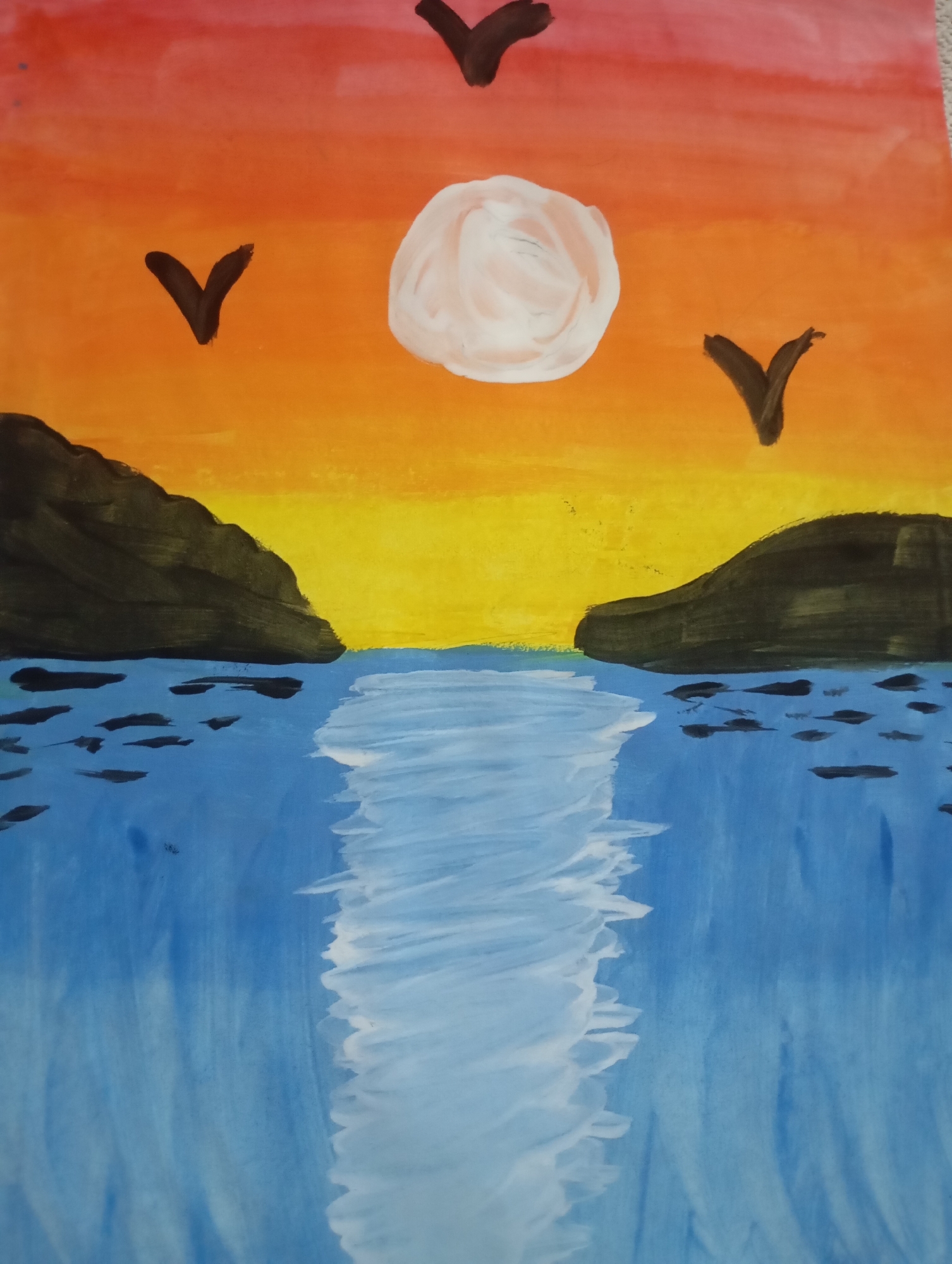 The image is a watercolor painting depicting a sunset over a body of water. Two dark, rocky landmasses frame a central channel of blue water, which reflects the bright yellow and orange hues of the sky. The sky transitions from red at the top to orange and then yellow towards the horizon. A pale, circular sun is visible in the upper center of the sky, with three dark, V-shaped birds in flight. Several dark, elongated shapes are scattered on the surface of the water, possibly representing boats or debris. The water exhibits white highlights, suggesting the reflection of the sun. The overall impression is a serene, natural landscape. The painting does not contain any elements that would place it specifically in Pirallahi Raion, Azerbaijan.