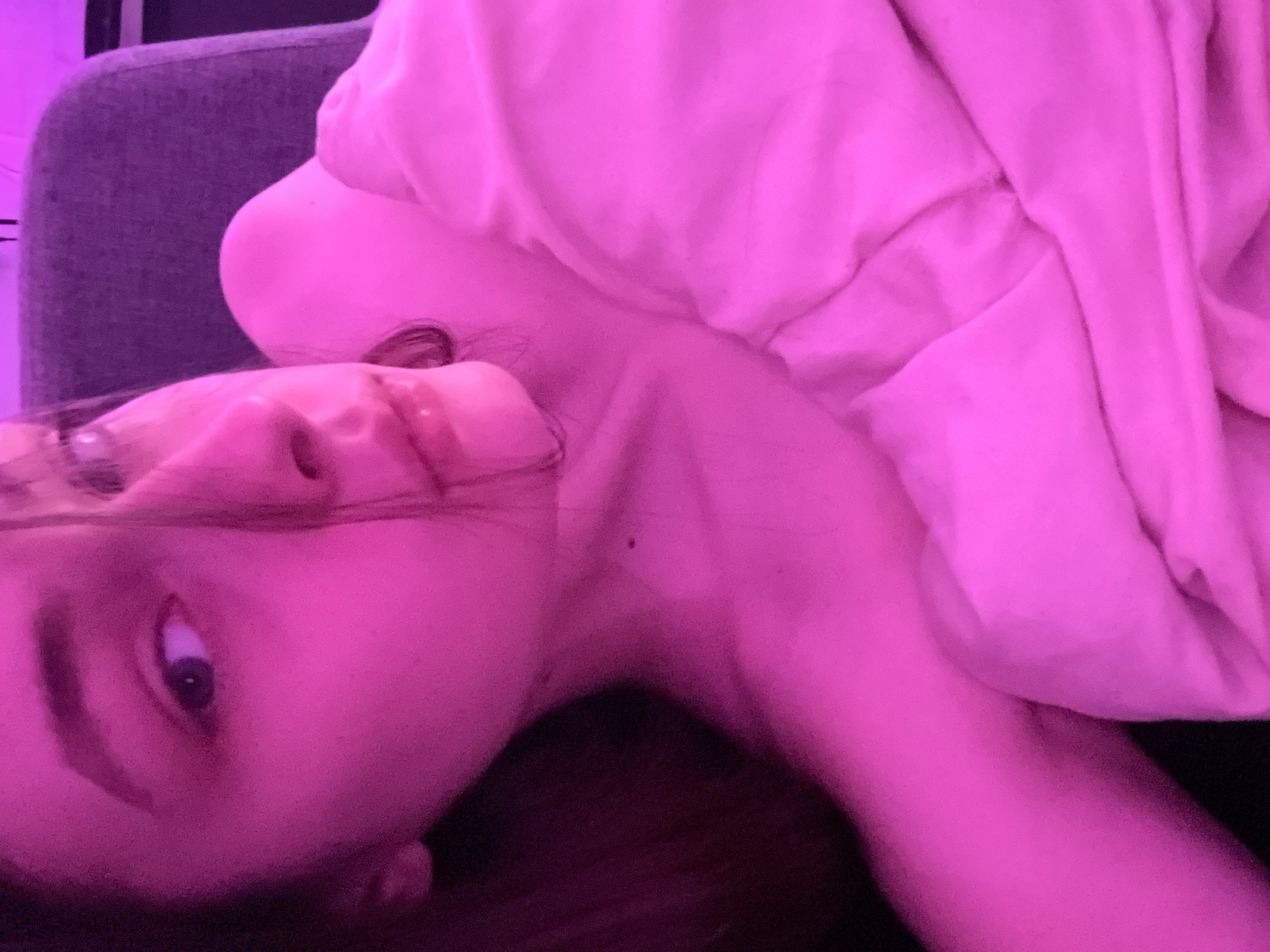 A person is lying down, wrapped in a light pink blanket. They are resting on a gray cushioned chair or couch. The lighting is predominantly pink. The location is not evident from the image and therefore, cannot be determined to be Saint Petersburg, Russia.