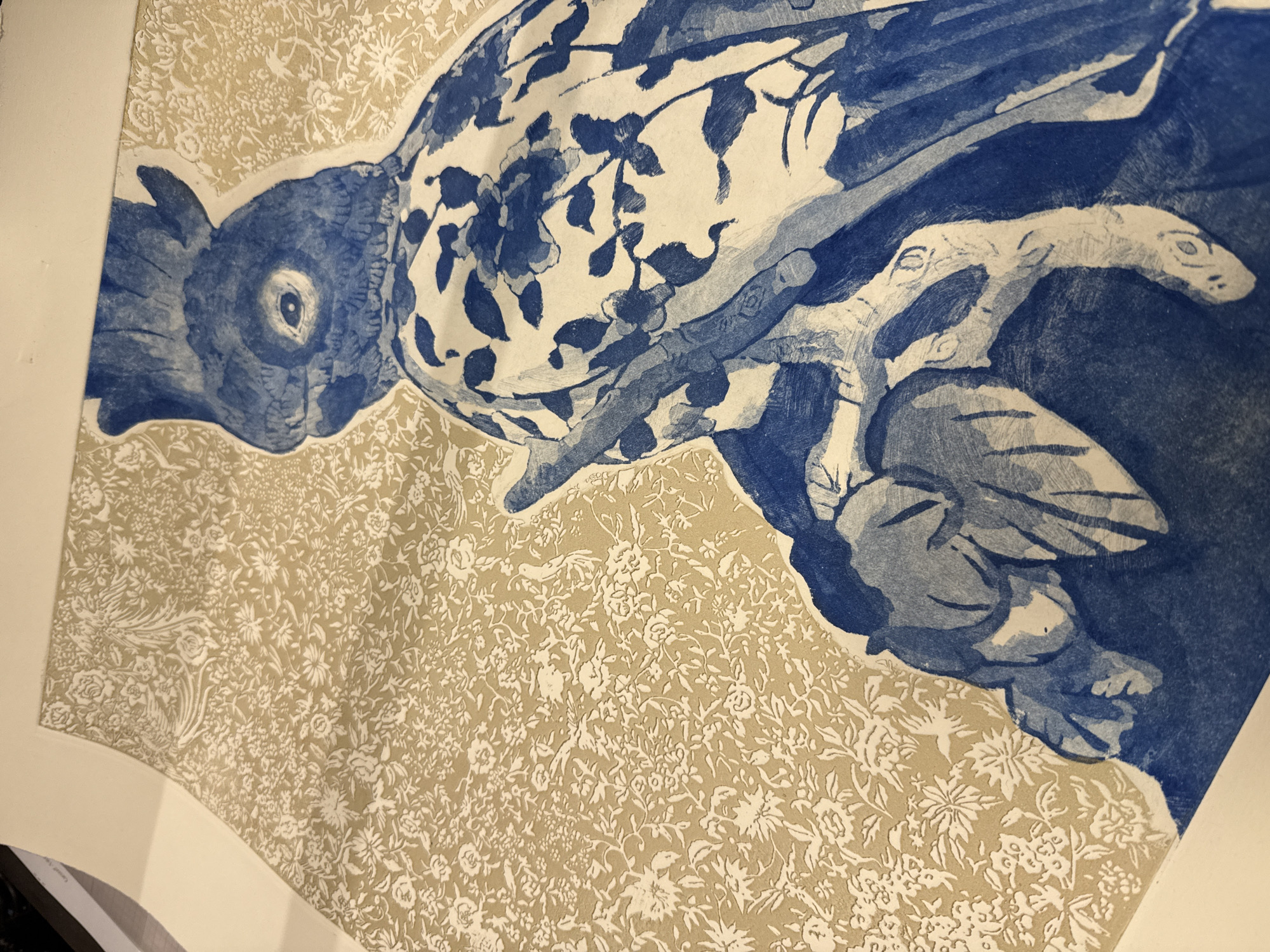 The image is a close-up of a print depicting a blue and white bird perched on a branch. The bird has detailed feathers and a distinctive eye. The branch appears to have leaves and flowers. The background is a floral pattern in a light tan color. It is possibly a piece of art, perhaps an etching or lithograph. There is no verifiable way to determine from this image where in Madrid, Spain, this print is located, or if it is even there.